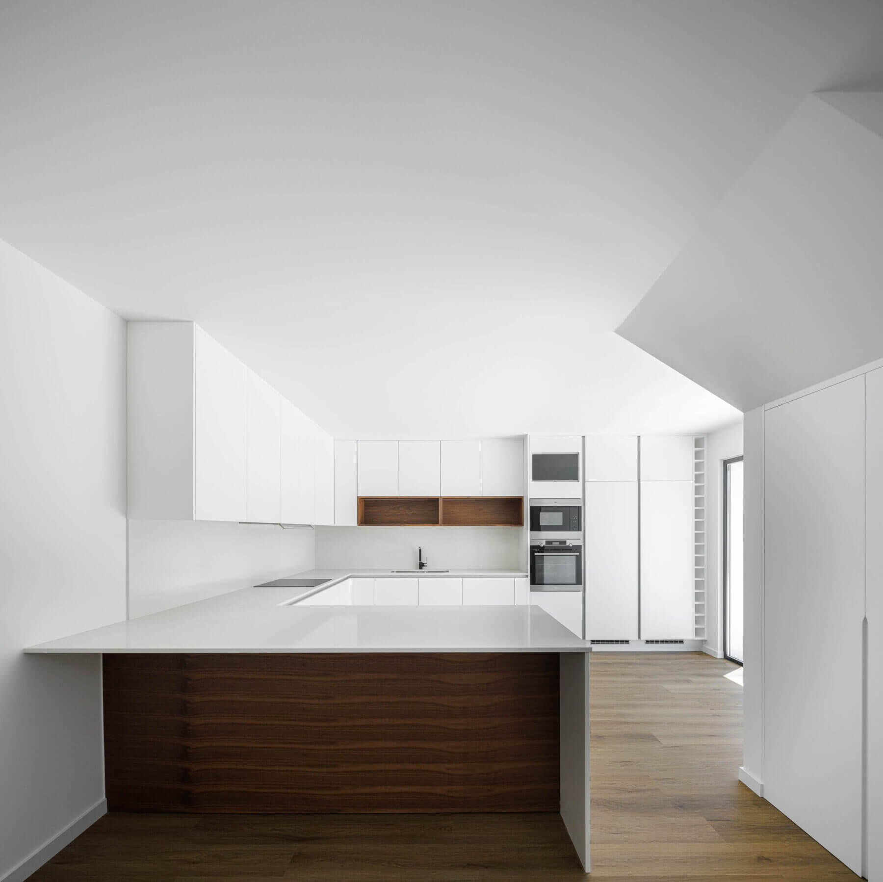 Cozinha: Perspectiva da cozinha com armários brancos, ilha central em madeira e eletrodomésticos embutidos. — Casas BD arquitetura Esquissos Arquitectura em Sintra
