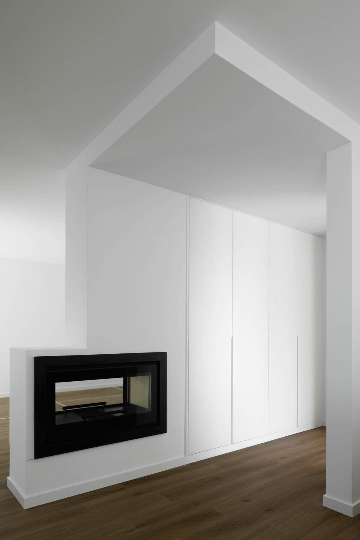 Sala de estar: Lareira embutida numa parede branca, com armários embutidos e pavimento em madeira. — Casas BD arquitetura Esquissos Arquitectura em Sintra