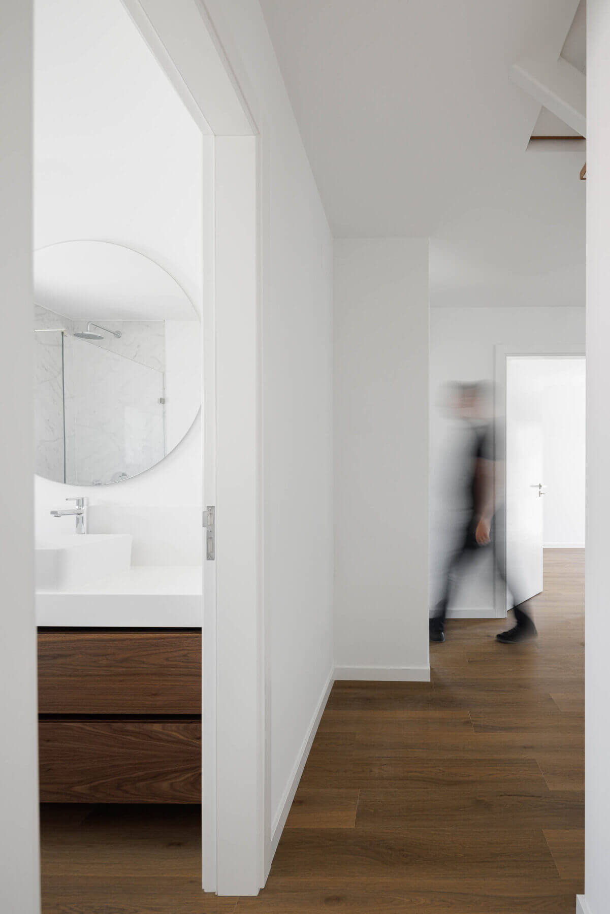 Casa de banho: Lavatório branco sobre móvel em madeira, espelho redondo e duche com resguardo em vidro. — Casas BD arquitetura Esquissos Arquitectura em Sintra