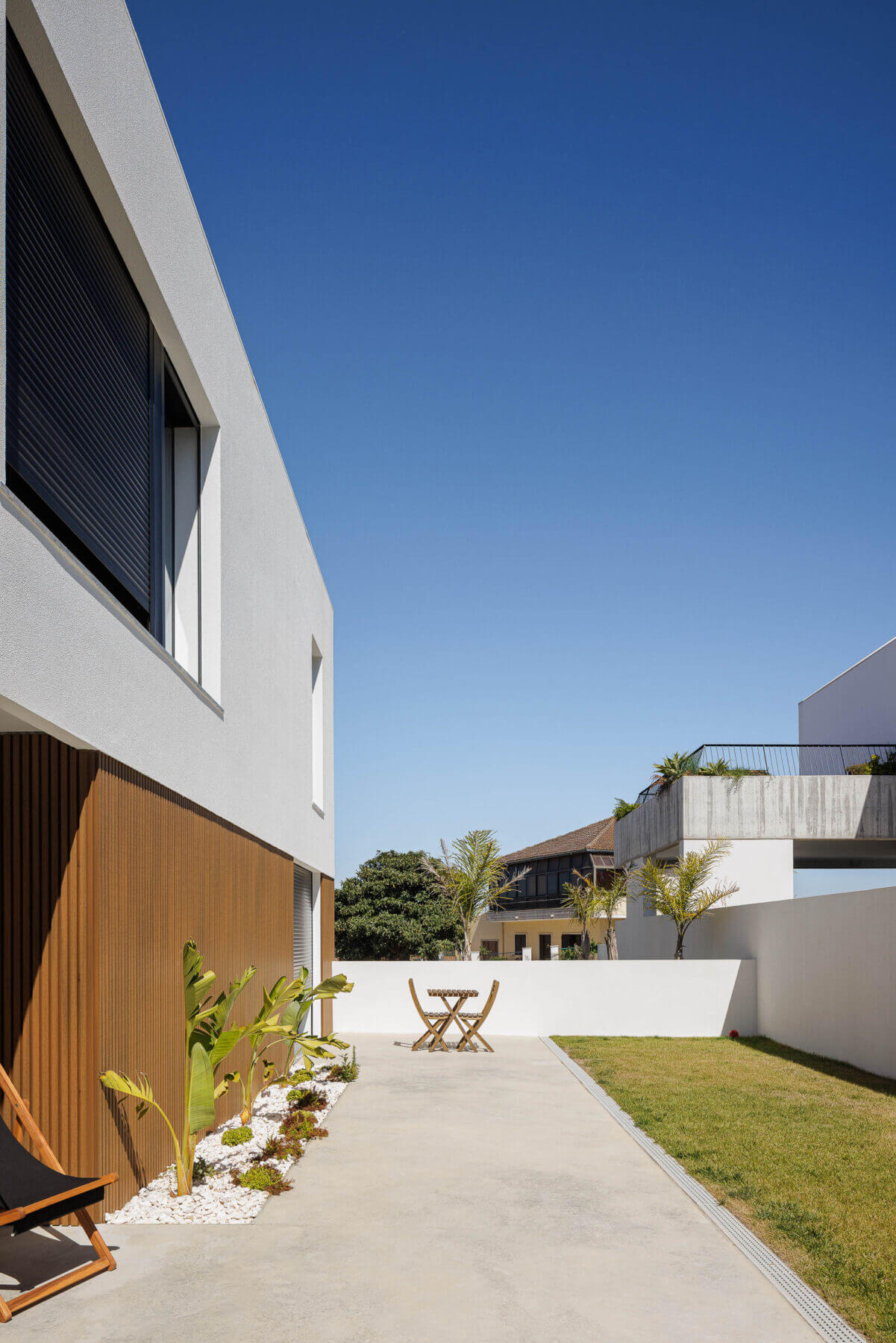 Fachada: Moradia branca com janela preta e anexo com porta em grelha metálica. — Casas BD arquitetura Esquissos Arquitectura em Sintra