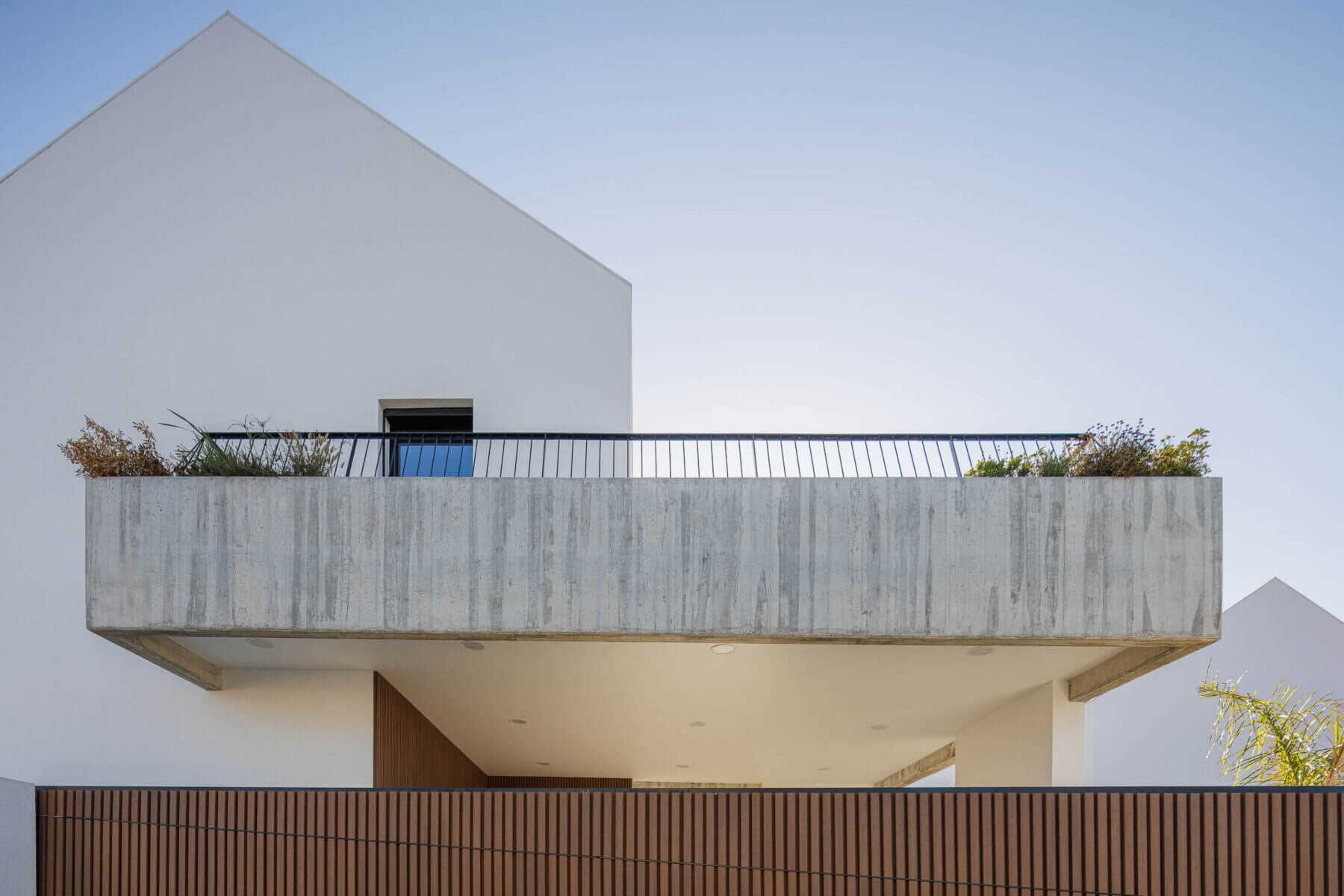 Fachada: Moradia branca com varanda em betão aparente e portão de madeira ripada. — Casas BD arquitetura Esquissos Arquitectura em Sintra