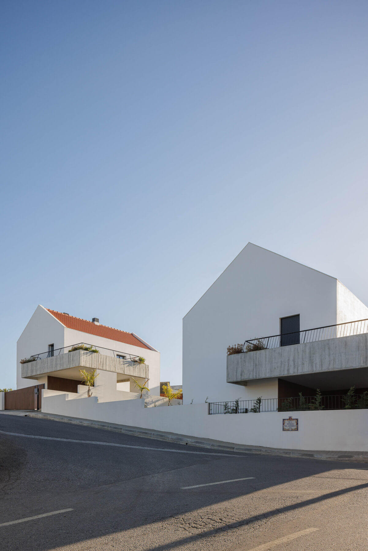 Fachada: Vista das moradias brancas com varandas em betão aparente e telhado cerâmico. — Casas BD arquitetura Esquissos Arquitectura em Sintra