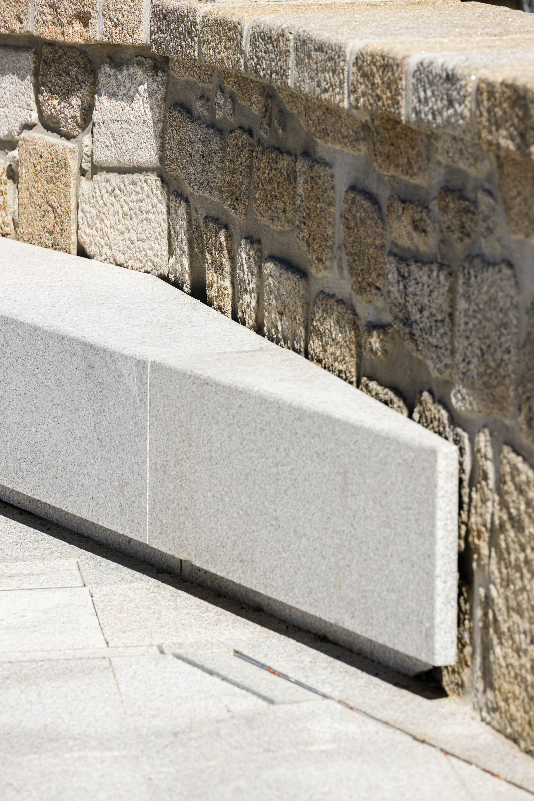 Praça: Banco em granito cinza claro encostado a muro de pedra rústica. — Requalificação da Praça do Município de Ribeira de Pena arquitetura AXR - Arquitetura e Design em Vila Real