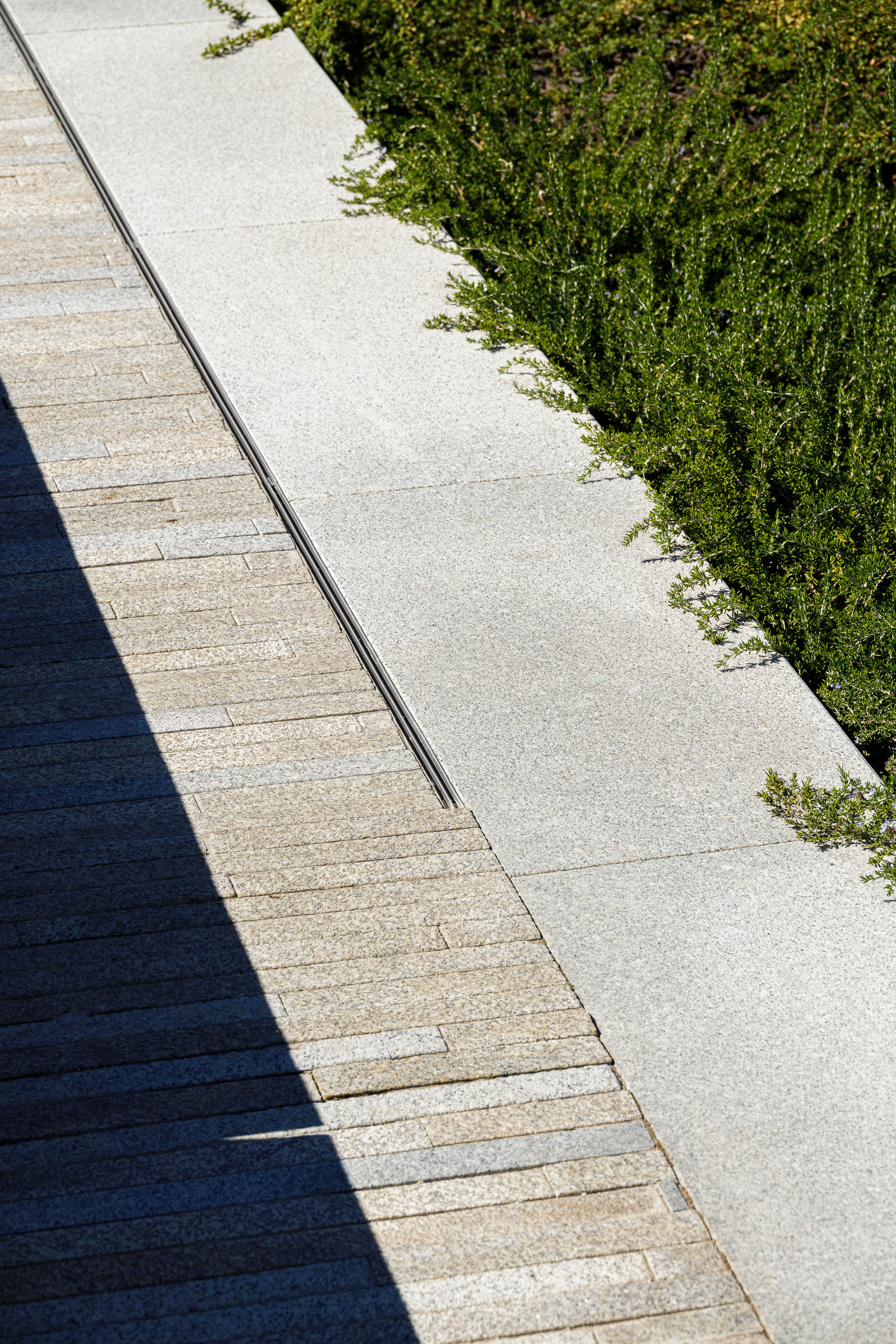 Praça: Canteiro com vegetação rasteira, delimitado por granito cinza claro e pavimento em pedra. — Requalificação da Praça do Município de Ribeira de Pena arquitetura AXR - Arquitetura e Design em Vila Real