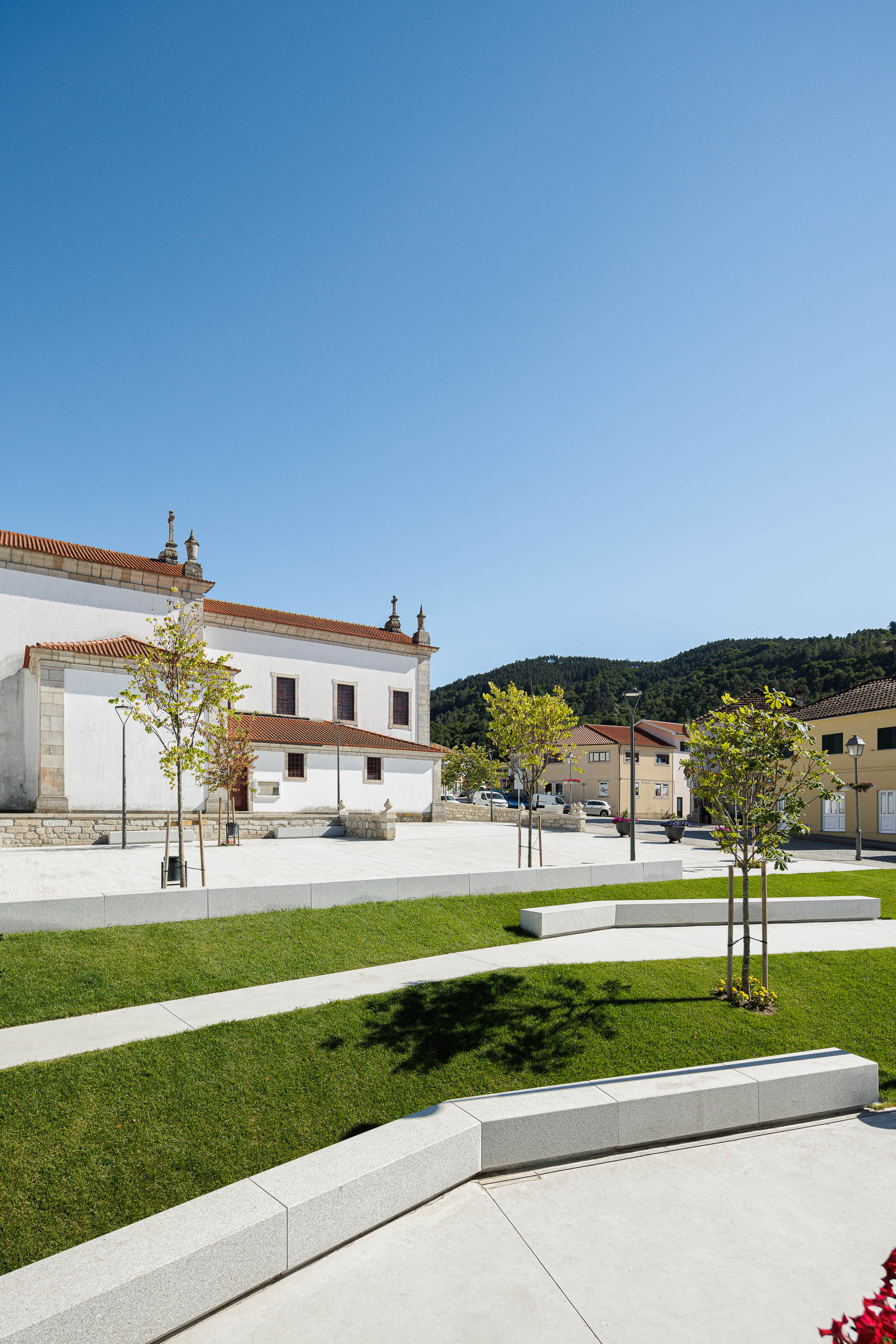 Praça: Igreja com relvado, bancos em granito e candeeiros modernos. — Requalificação da Praça do Município de Ribeira de Pena arquitetura AXR - Arquitetura e Design em Vila Real