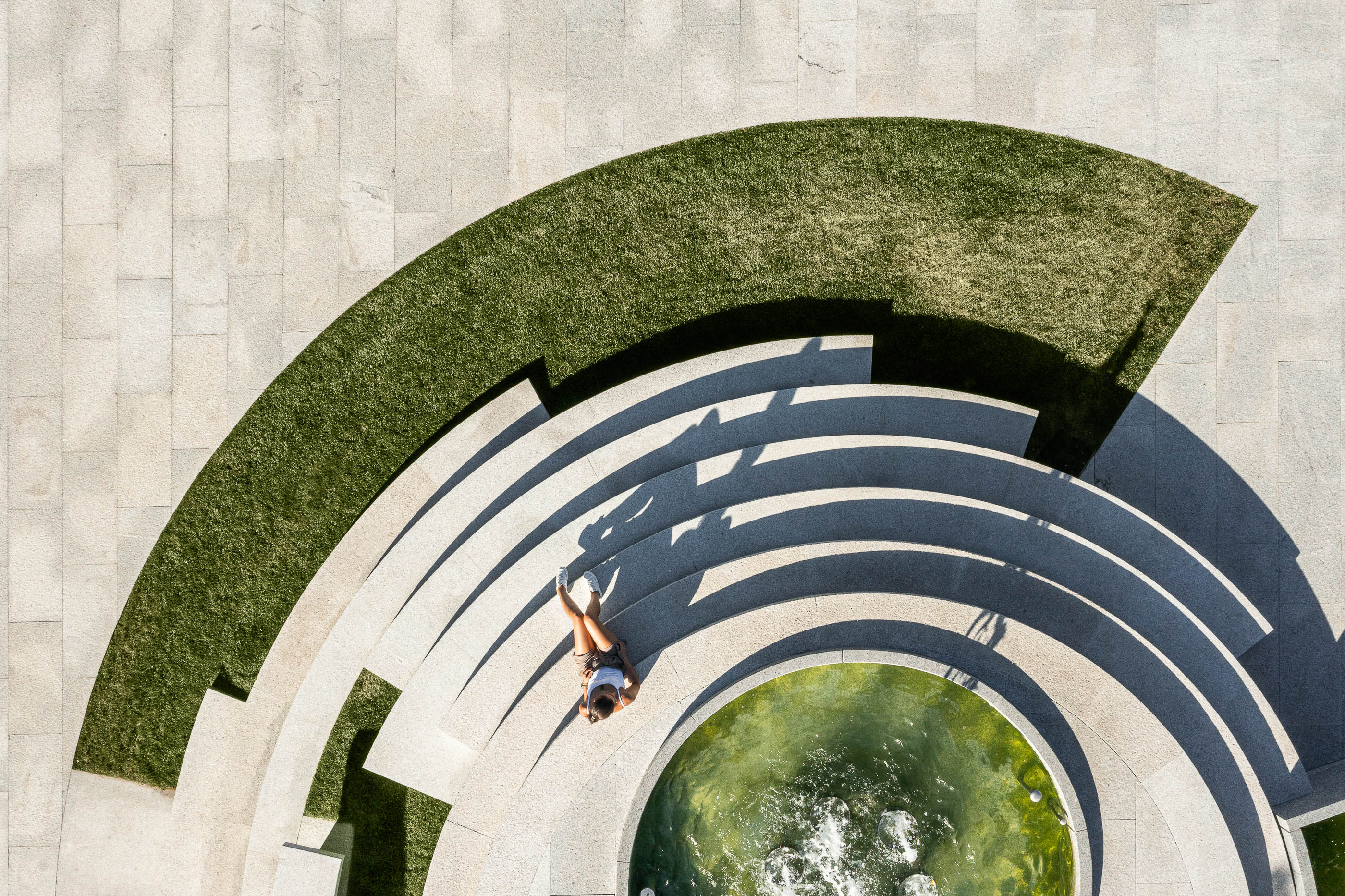 Praça: Vista aérea da fonte escalonada com relvado e pessoas a relaxar. — Requalificação da Praça do Município de Ribeira de Pena arquitetura AXR - Arquitetura e Design em Vila Real