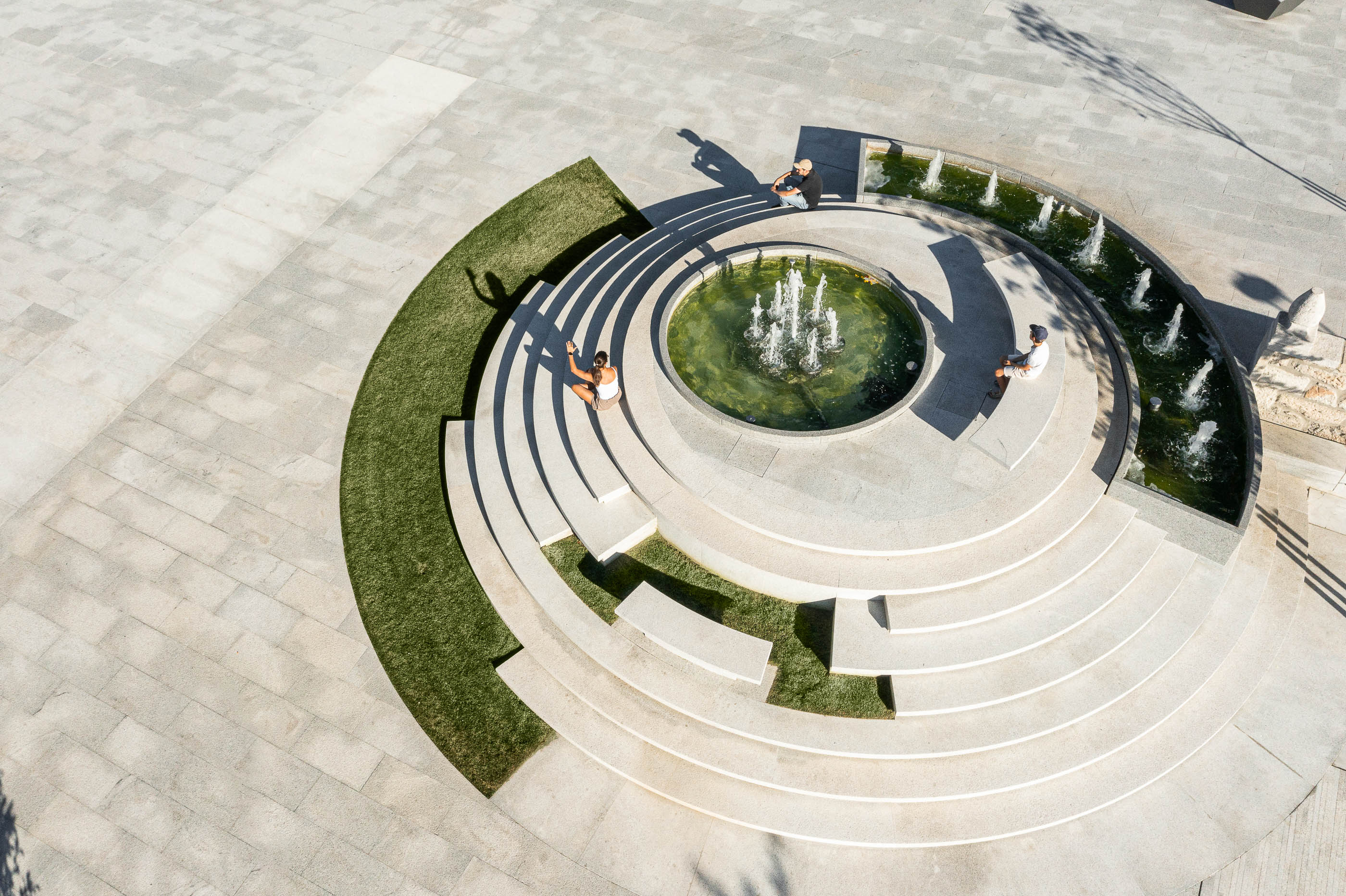 Praça: Vista aérea da fonte escalonada com relvado e pessoas a relaxar. — Requalificação da Praça do Município de Ribeira de Pena arquitetura AXR - Arquitetura e Design em Vila Real