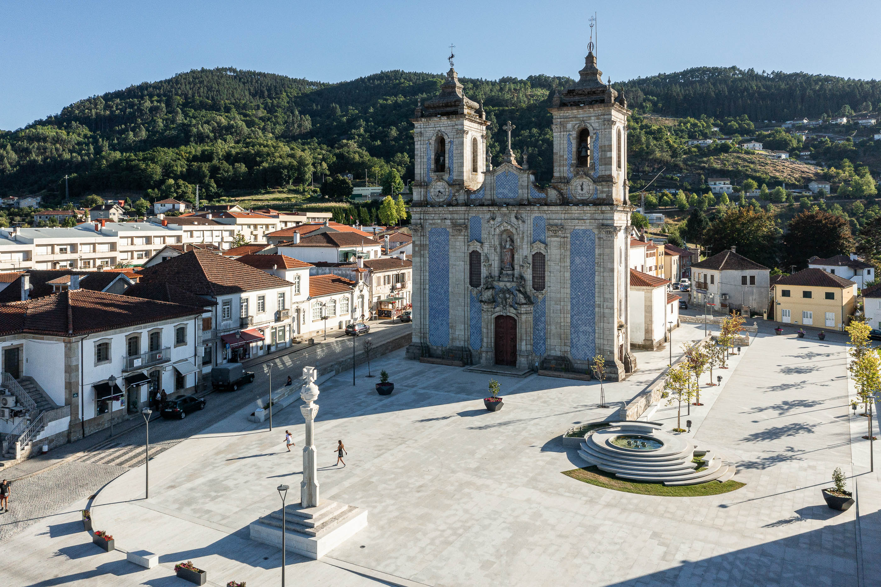 Praça: Vista geral da praça com igreja, cruzeiro e fonte escalonada. — Requalificação da Praça do Município de Ribeira de Pena arquitetura AXR - Arquitetura e Design em Vila Real