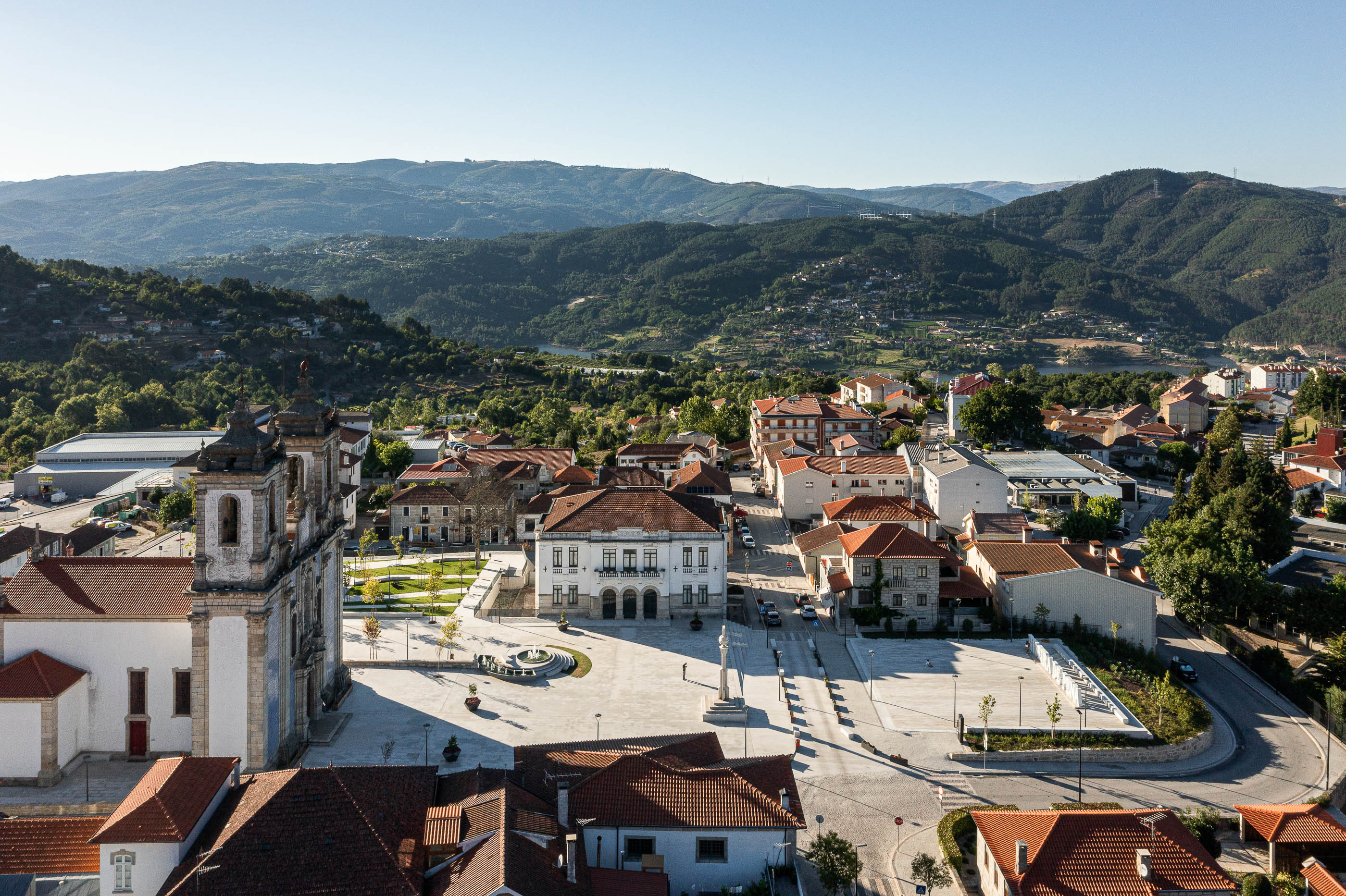Praça: Vista geral da vila com a praça central, igreja e edifícios com telhados de cor laranja. — Requalificação da Praça do Município de Ribeira de Pena arquitetura AXR - Arquitetura e Design em Vila Real
