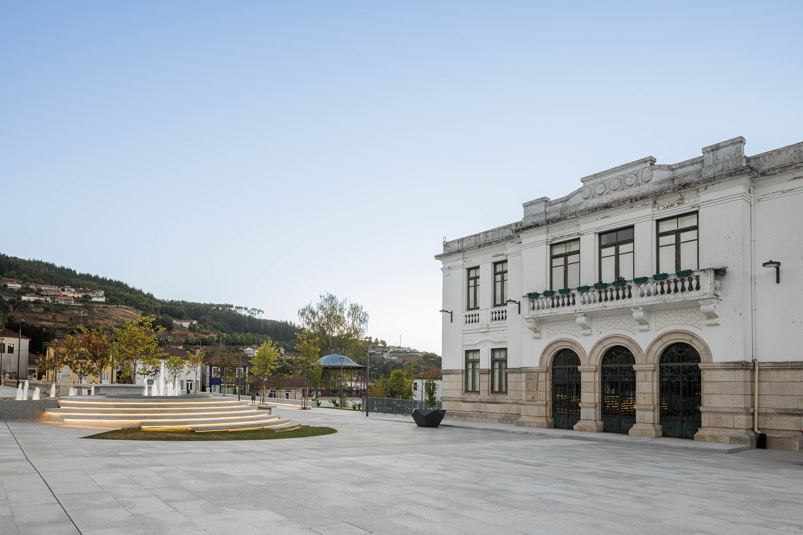 Praça: Edifício histórico, fonte escalonada e coreto. Pavimento em granito cinza claro. — Requalificação da Praça do Município de Ribeira de Pena arquitetura AXR - Arquitetura e Design em Vila Real