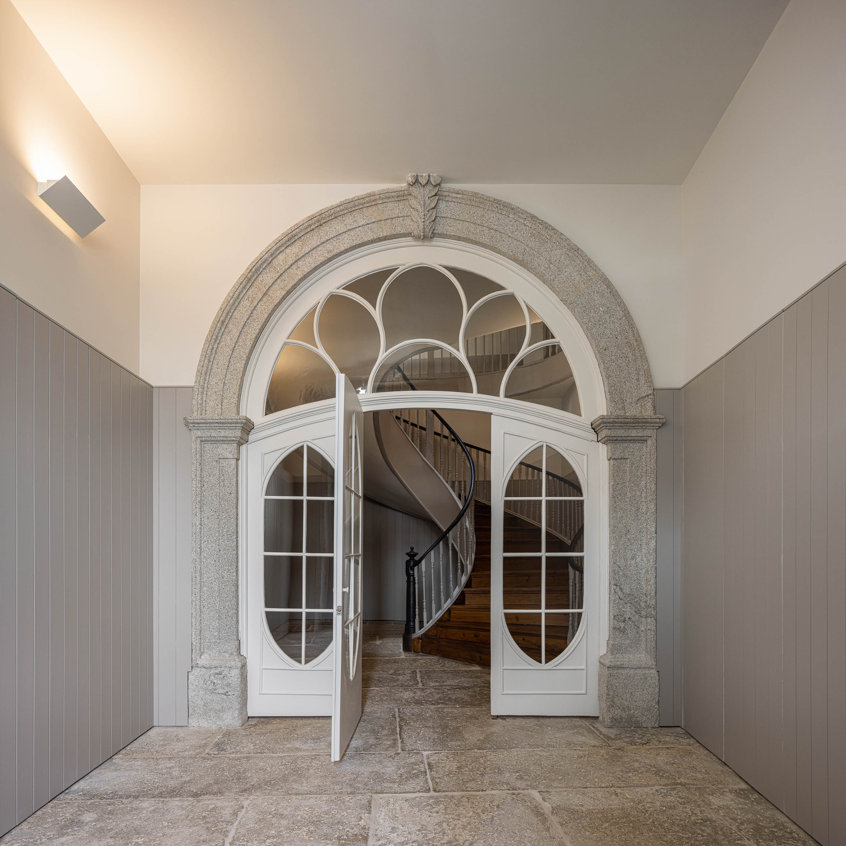 Entrada: Porta dupla em arco com caixilharia branca, pavimento em pedra rústica e lambris cinza. — Antigo Hotel do Louvre arquitetura Diana Barros Arquitectura em Porto