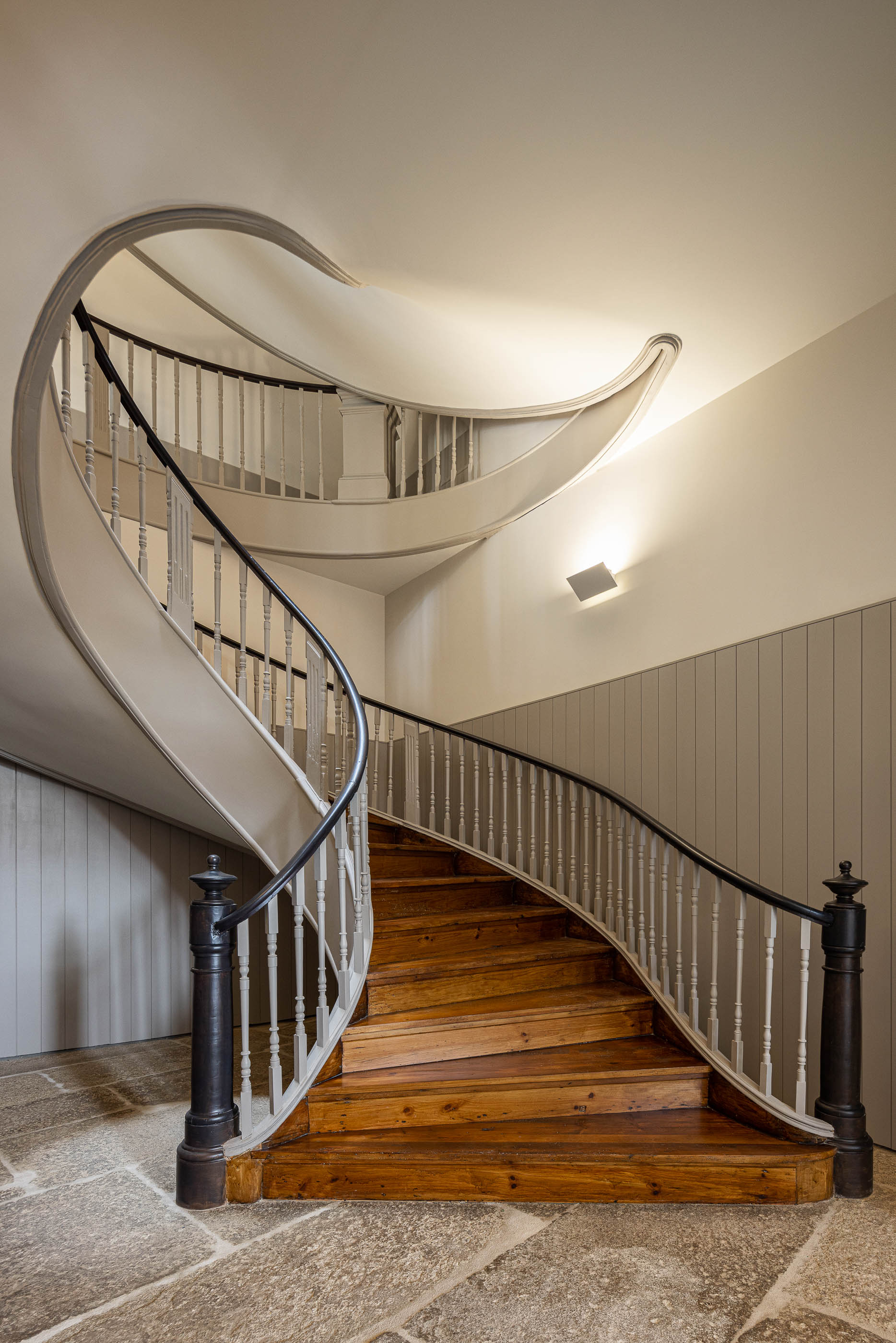 Escadaria: Escadaria em caracol com degraus de madeira e corrimão preto, paredes em tons neutros. — Antigo Hotel do Louvre arquitetura Diana Barros Arquitectura em Porto
