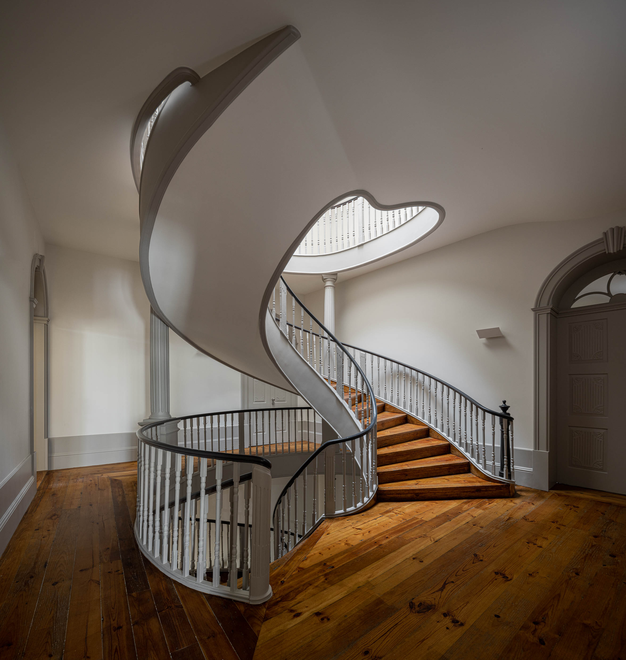 Escadaria: Vista geral da escadaria em caracol com claraboia, pavimento em madeira e portas em arco. — Antigo Hotel do Louvre arquitetura Diana Barros Arquitectura em Porto
