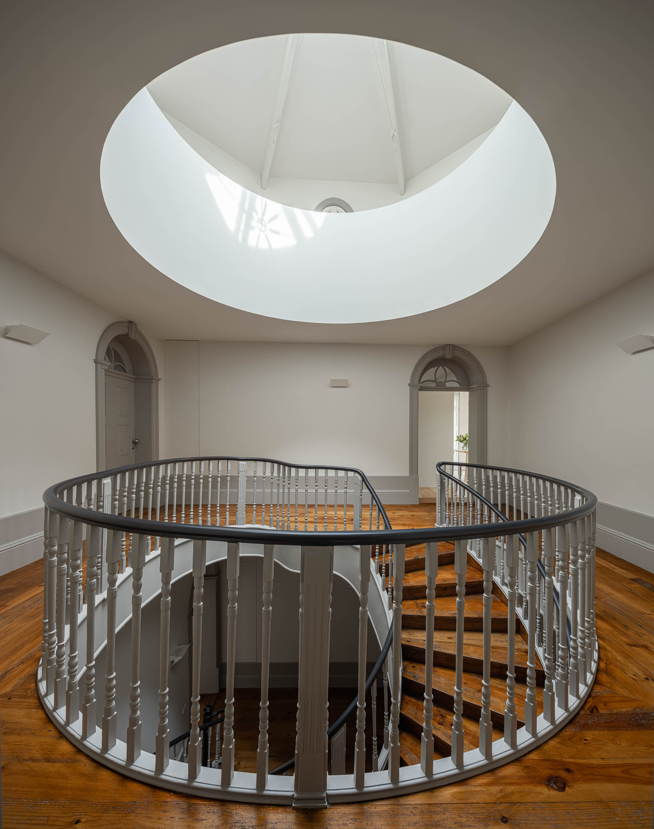 Hall: Corrimão da escadaria em caracol, pavimento em madeira e portas em arco ao fundo. — Antigo Hotel do Louvre arquitetura Diana Barros Arquitectura em Porto