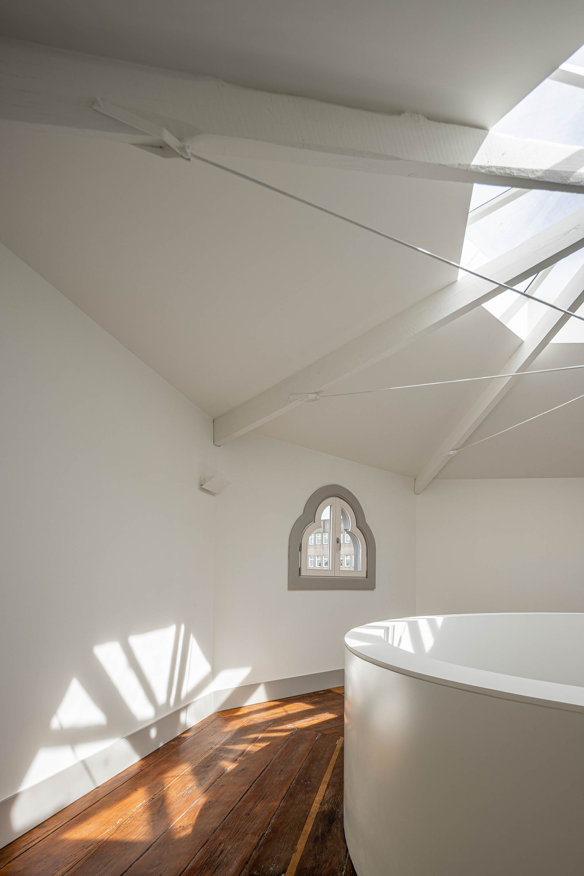 Sótão: Sótão com claraboia, vigas de madeira pintadas de branco e pavimento em madeira. — Antigo Hotel do Louvre arquitetura Diana Barros Arquitectura em Porto