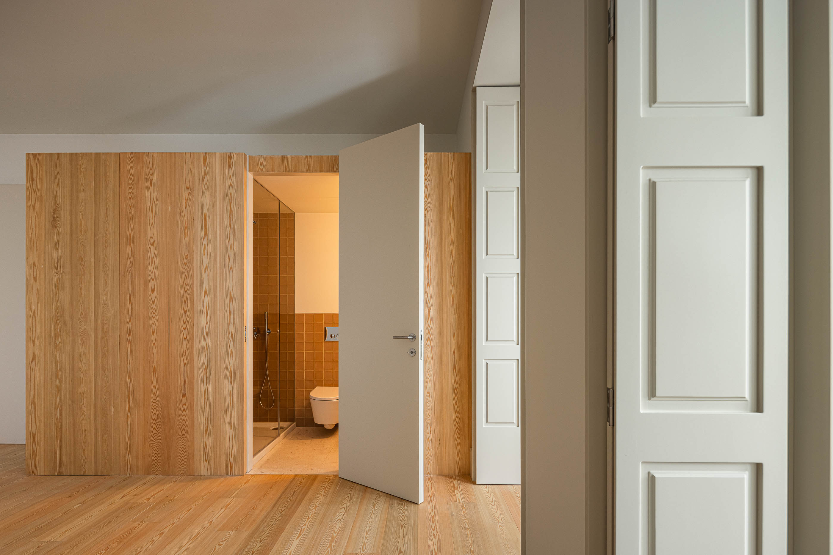 Casa de banho: Porta aberta para a casa de banho com azulejos rústicos e sanita suspensa. — Antigo Hotel do Louvre arquitetura Diana Barros Arquitectura em Porto
