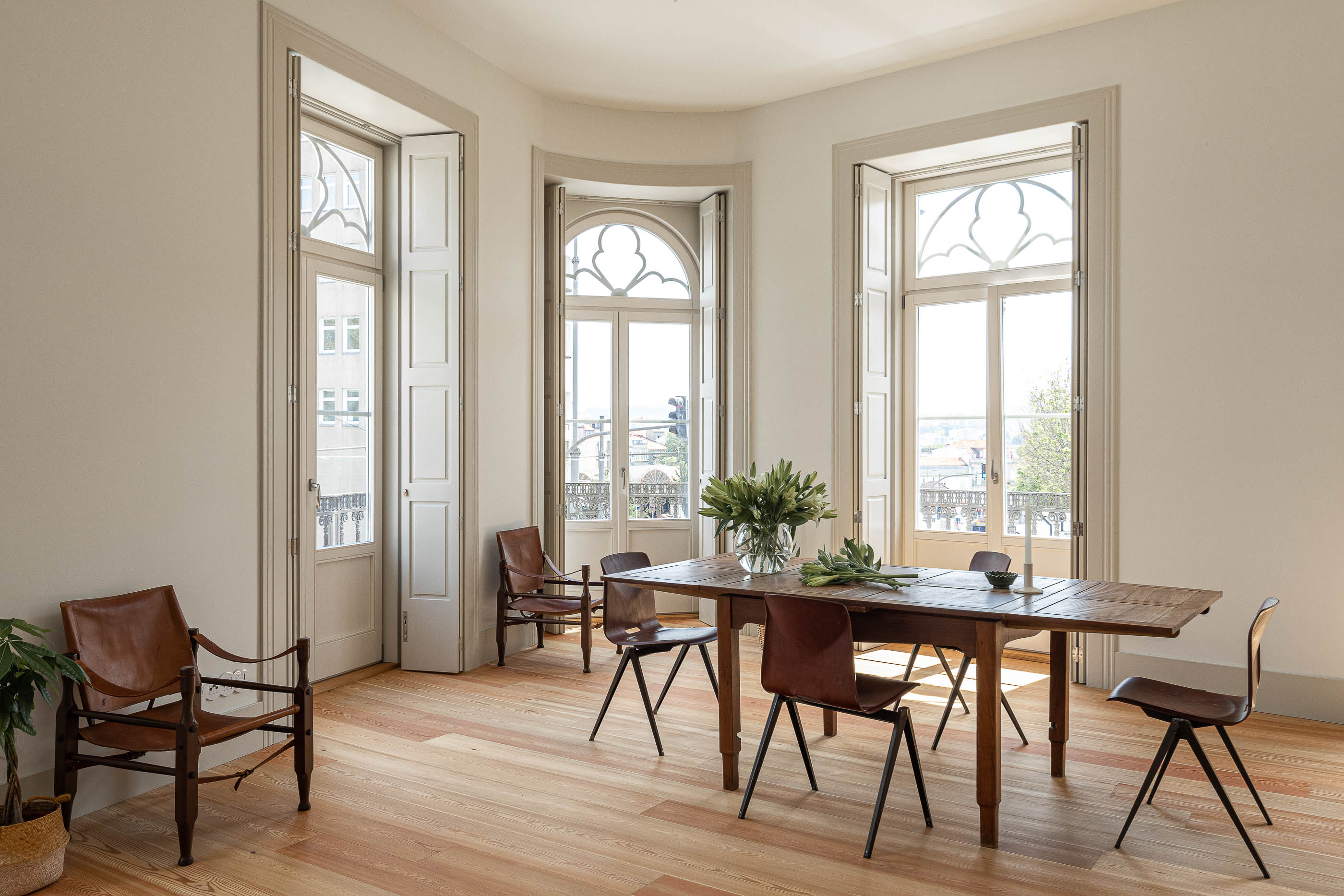 Sala de jantar: Sala de jantar com janelas em arco, mesa de madeira rústica e cadeiras de design. — Antigo Hotel do Louvre arquitetura Diana Barros Arquitectura em Porto