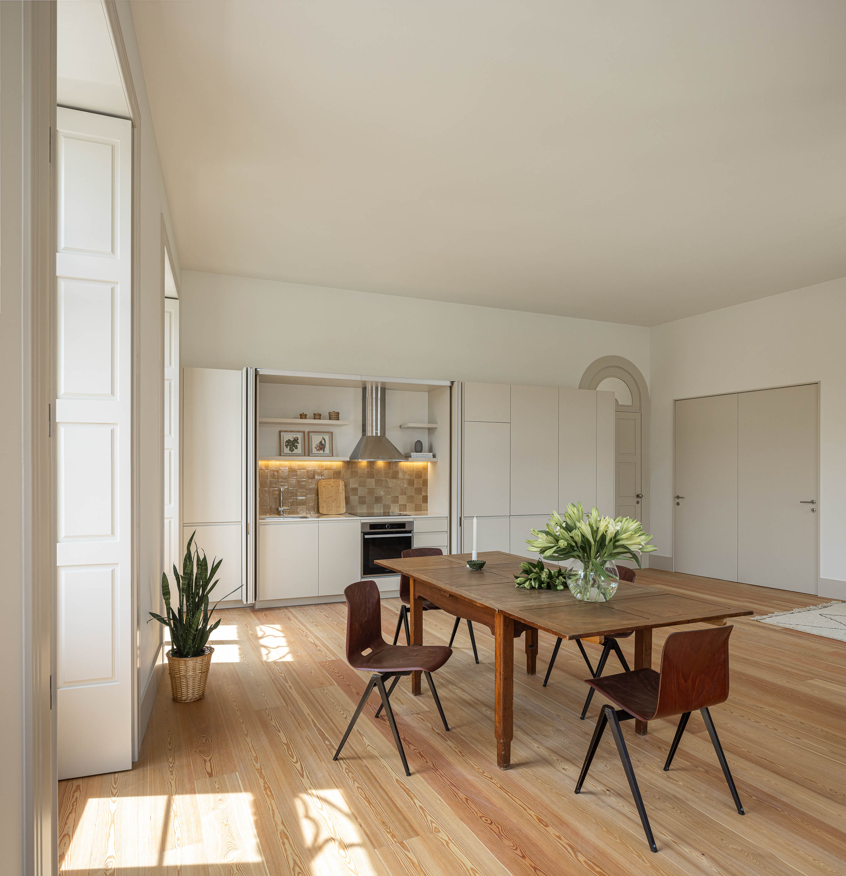 Sala de jantar: Sala de jantar com cozinha integrada, janelas em arco e pavimento em madeira. — Antigo Hotel do Louvre arquitetura Diana Barros Arquitectura em Porto