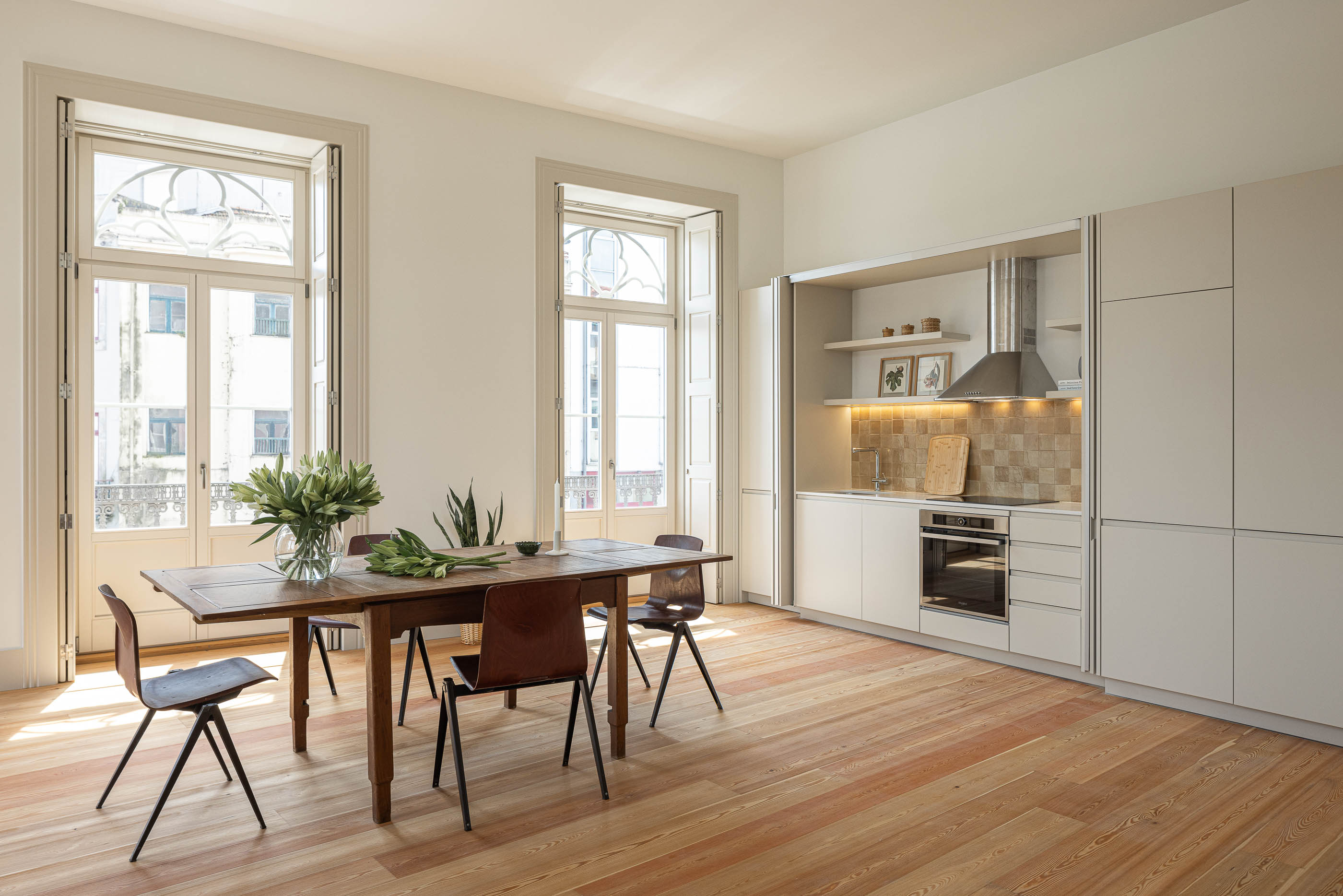 Sala de jantar: Sala de jantar com cozinha moderna, janelas em arco e mesa de madeira rústica. — Antigo Hotel do Louvre arquitetura Diana Barros Arquitectura em Porto