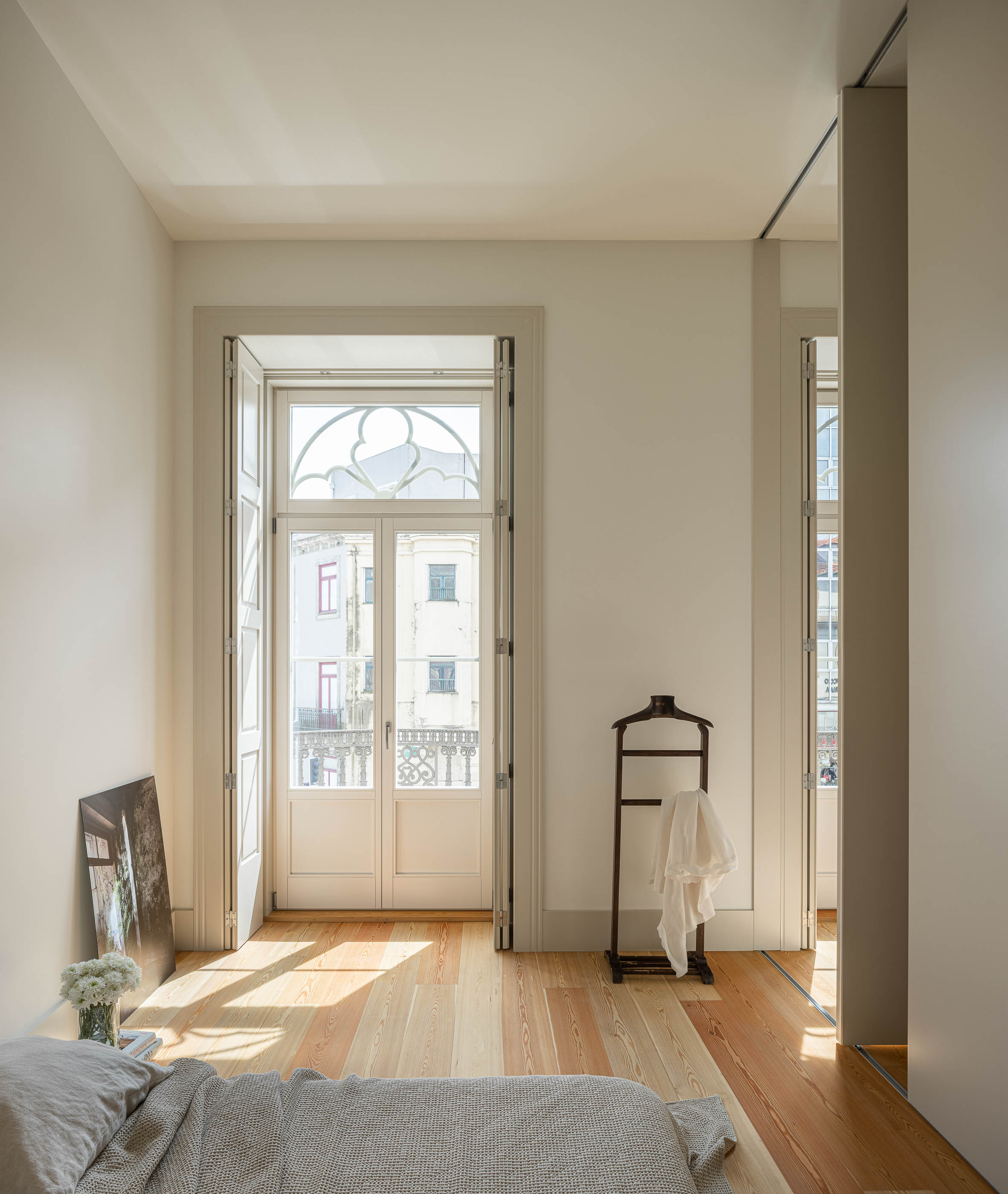Quarto: Quarto com divisórias de correr, janela em arco e cabideiro com roupa branca. — Antigo Hotel do Louvre arquitetura Diana Barros Arquitectura em Porto
