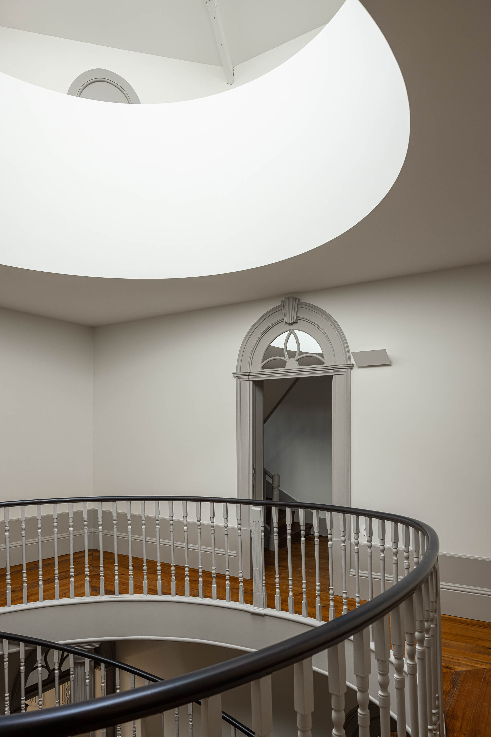 Hall: Corrimão da escadaria em caracol, porta em arco e claraboia ao fundo. — Antigo Hotel do Louvre arquitetura Diana Barros Arquitectura em Porto