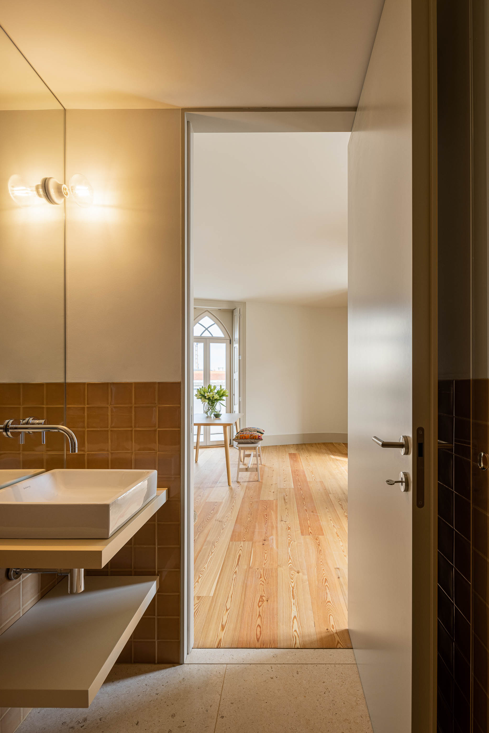 Casa de banho: Casa de banho com lavatório branco, azulejos rústicos e porta para o quarto. — Antigo Hotel do Louvre arquitetura Diana Barros Arquitectura em Porto