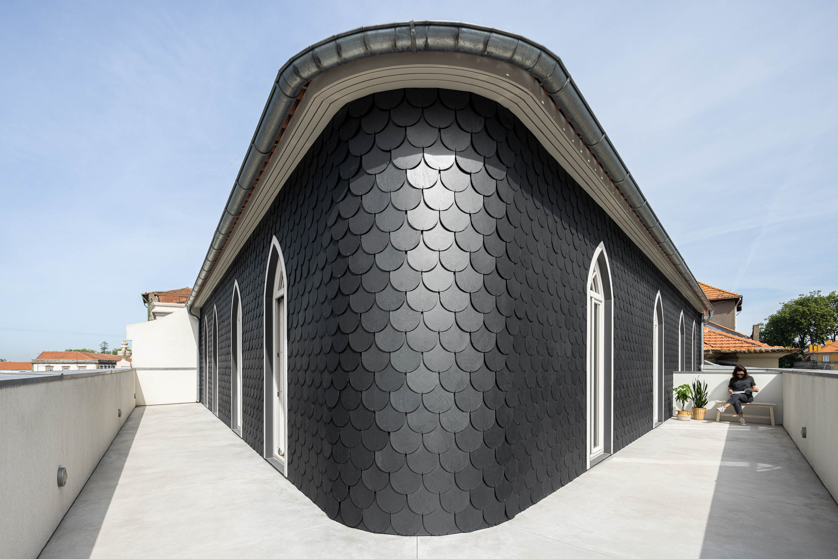 Terraço: Fachada do edifício revestida a escamas pretas, com janelas em arco e terraço em betão. — Antigo Hotel do Louvre arquitetura Diana Barros Arquitectura em Porto