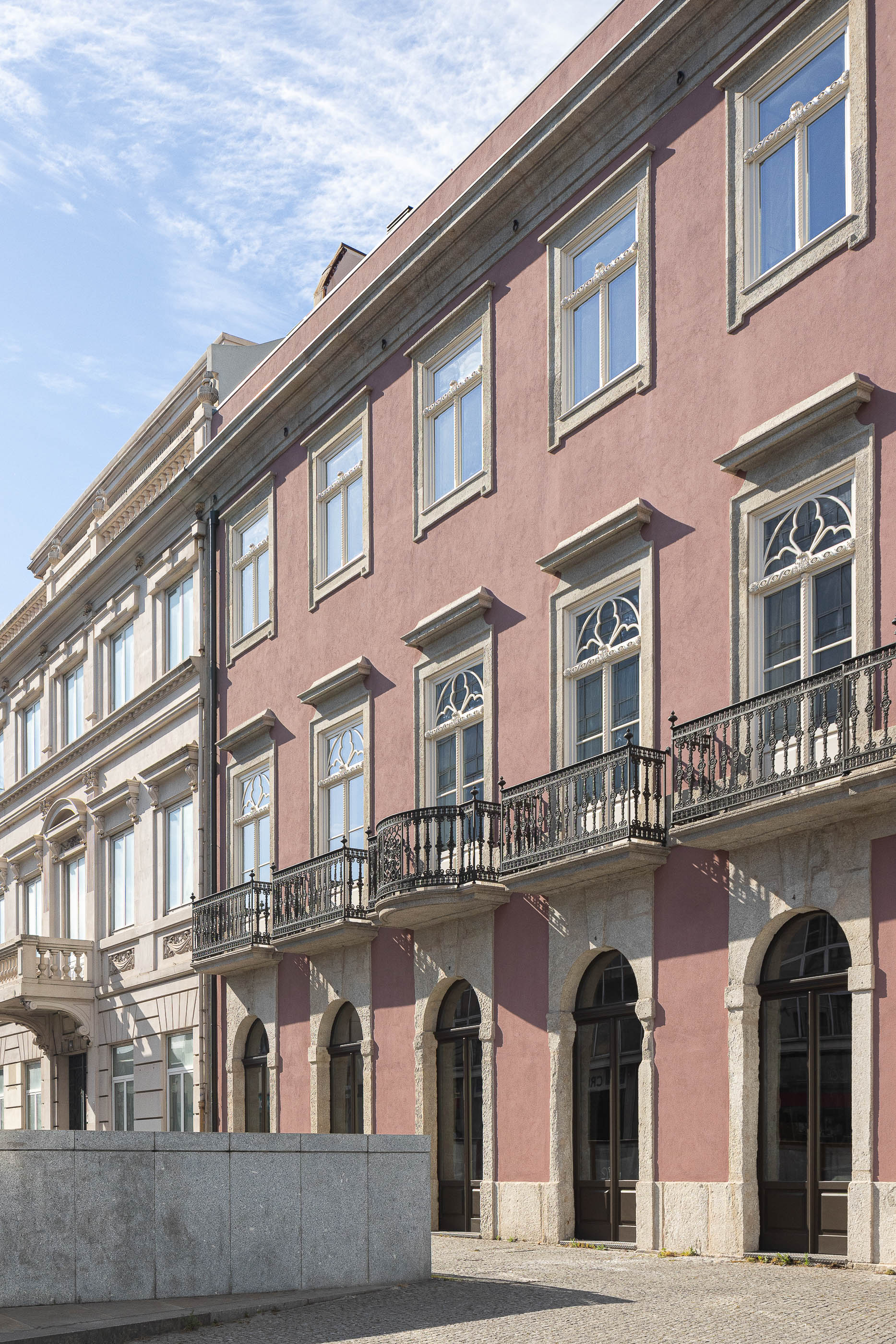 Exterior: Vista lateral da fachada do edifício rosa com janelas em arco e varandas em ferro forjado. — Antigo Hotel do Louvre arquitetura Diana Barros Arquitectura em Porto