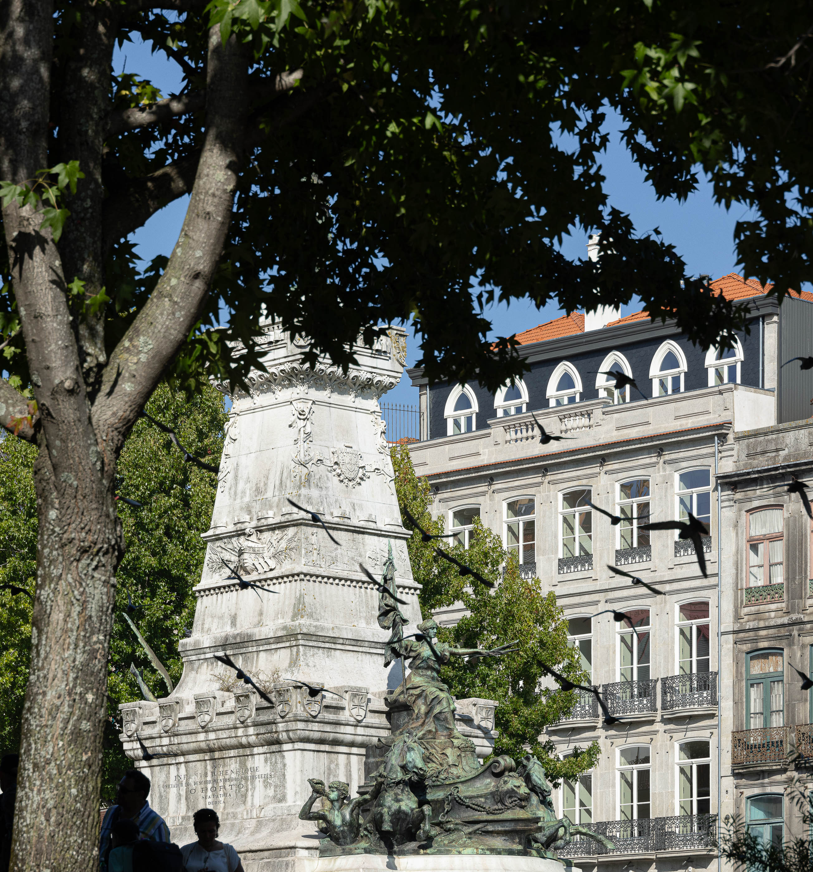 Exterior: Monumento na praça com o edifício renovado ao fundo, com janelas em arco. — Edifício de Mouzinho da Silveira arquitetura Diana Barros Arquitectura em Porto