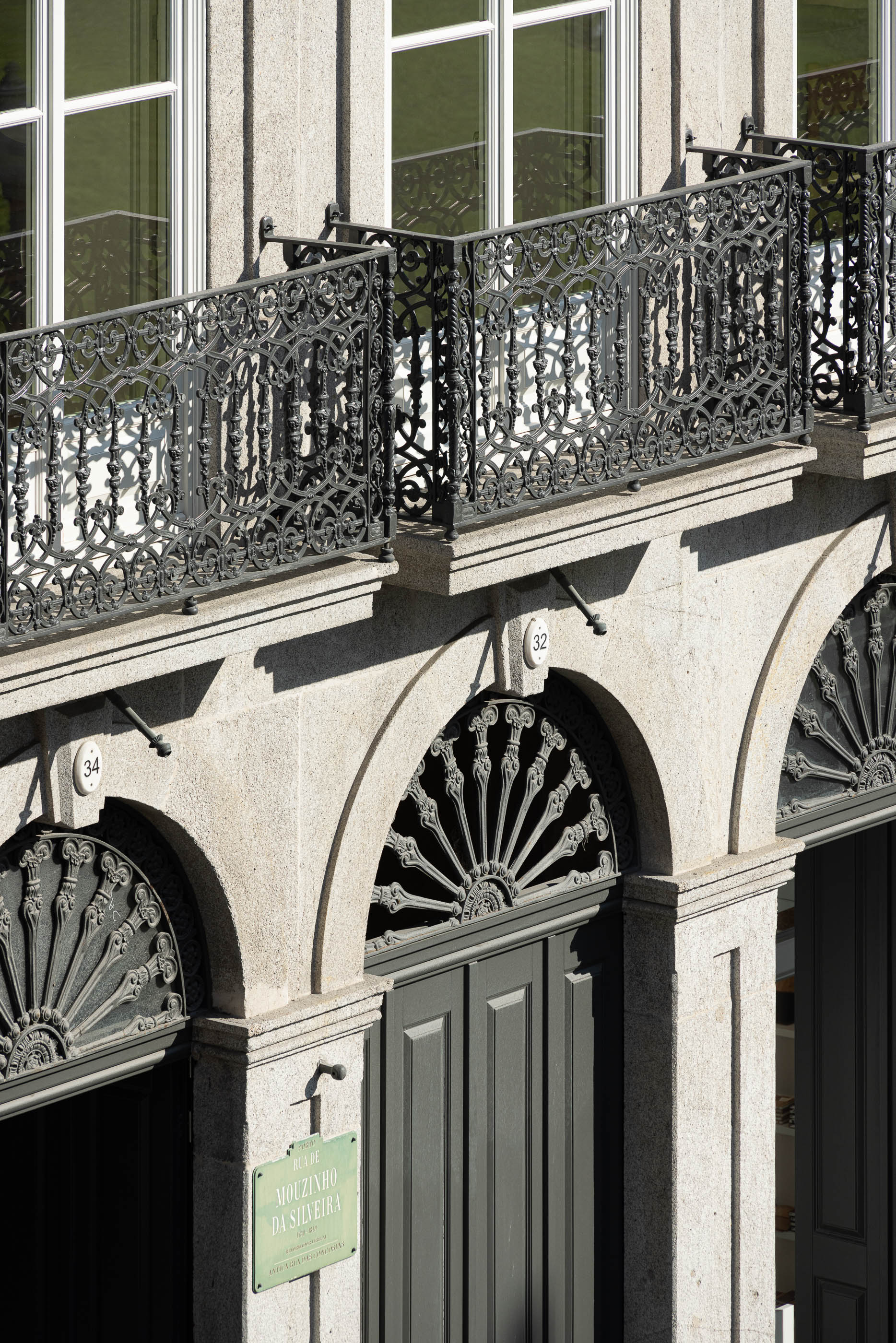 Entrada: Detalhe da fachada com portas de madeira escura, gradeamento em arco e placa identificativa. — Edifício de Mouzinho da Silveira arquitetura Diana Barros Arquitectura em Porto