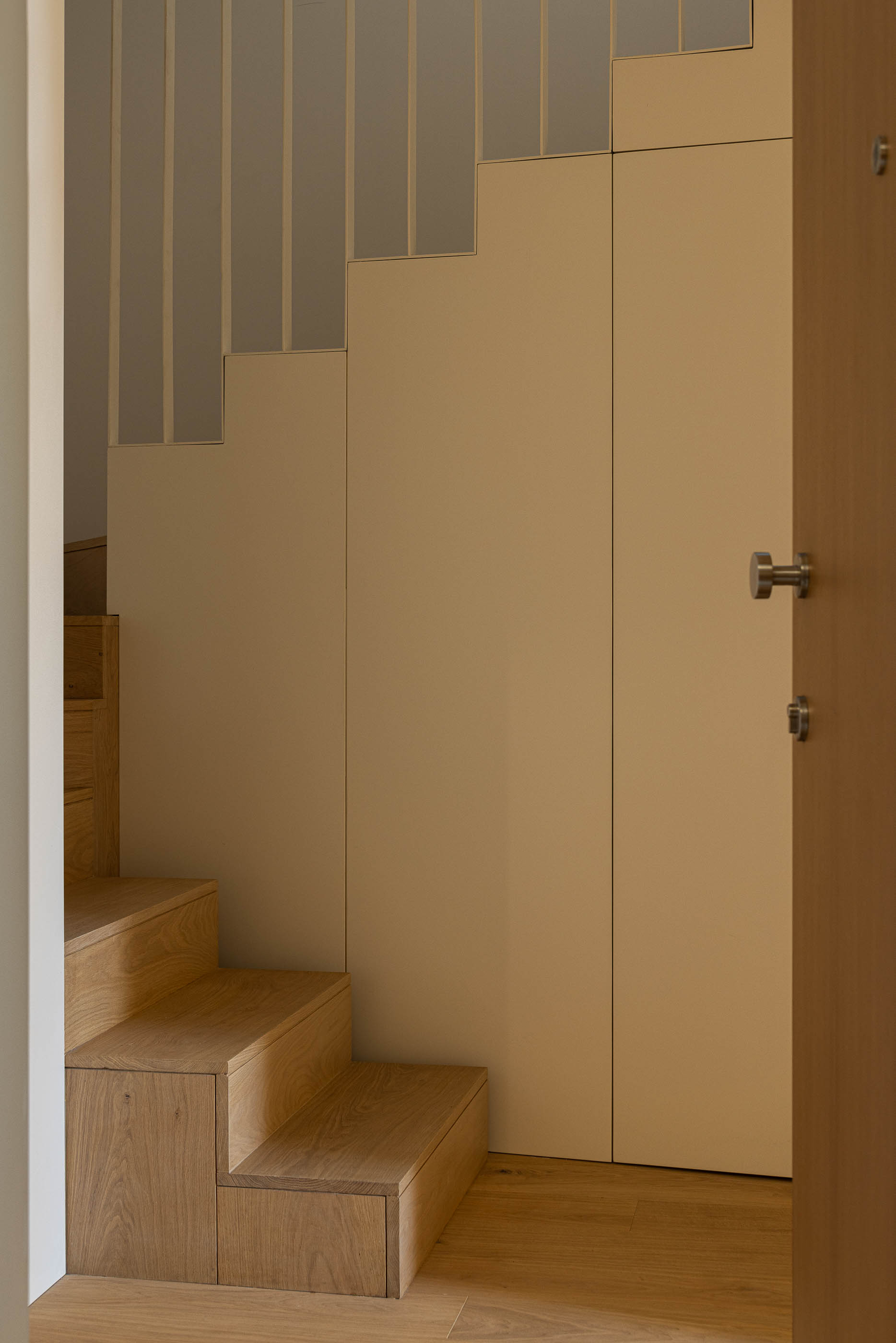 Escadas: Detalhe dos degraus em madeira clara com armários embutidos e corrimão branco. — Edifício de Mouzinho da Silveira arquitetura Diana Barros Arquitectura em Porto