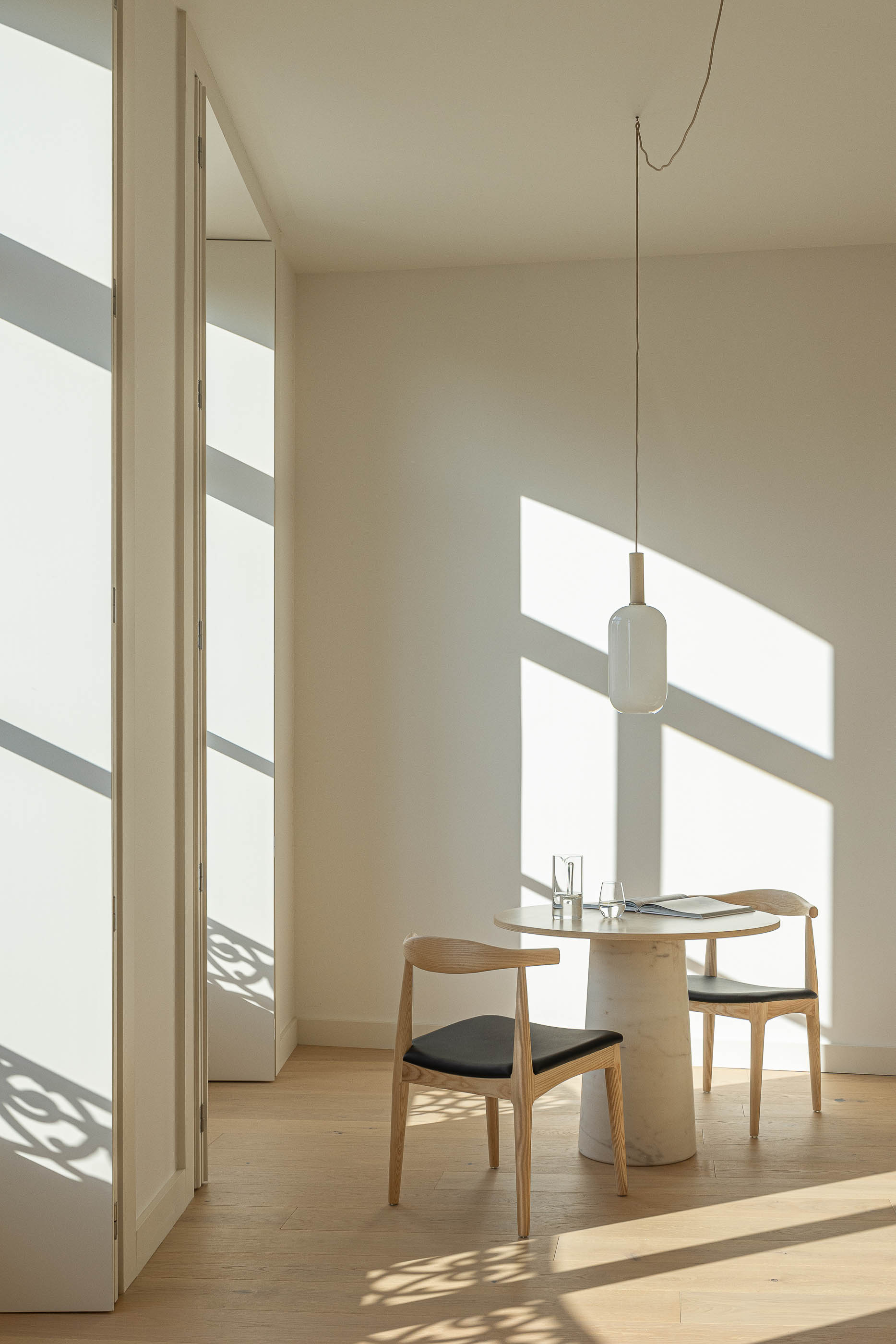 Sala de jantar: Mesa redonda com cadeiras de madeira, candeeiro suspenso e portadas dobráveis. — Edifício de Mouzinho da Silveira arquitetura Diana Barros Arquitectura em Porto