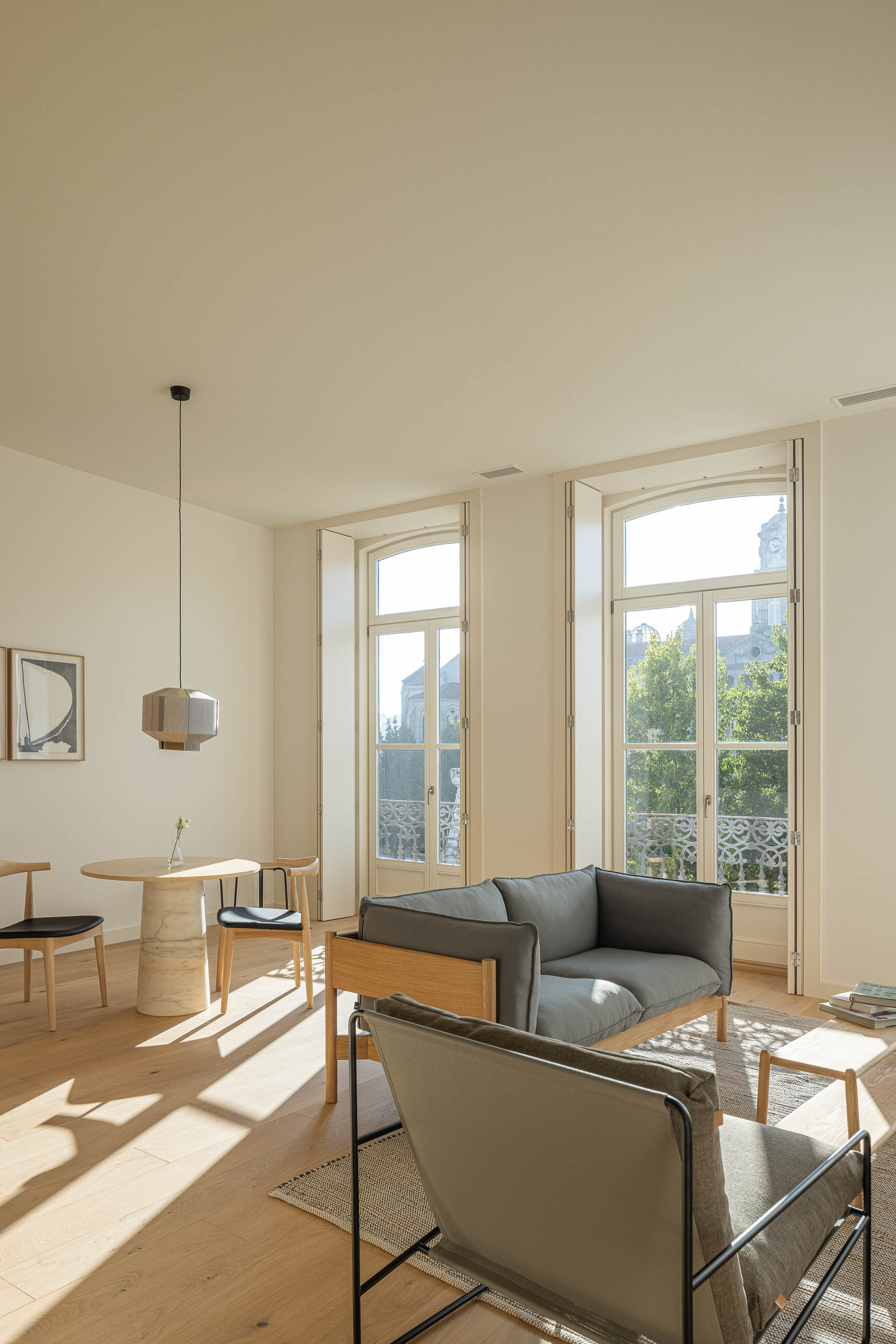 Sala de estar: Sofá cinzento, cadeiras de madeira e mesa redonda com candeeiro suspenso. — Edifício de Mouzinho da Silveira arquitetura Diana Barros Arquitectura em Porto
