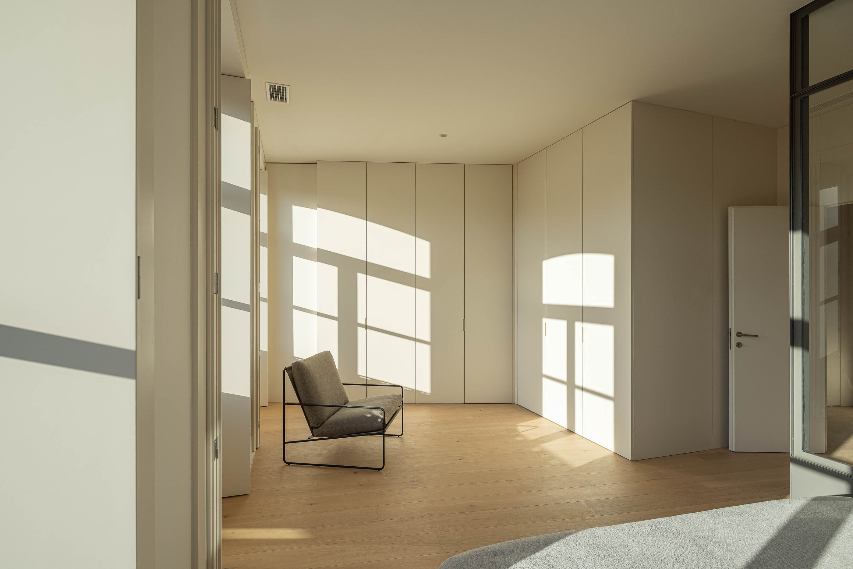 Quarto: Quarto com roupeiros embutidos brancos, cadeira e pavimento em madeira clara. — Edifício de Mouzinho da Silveira arquitetura Diana Barros Arquitectura em Porto