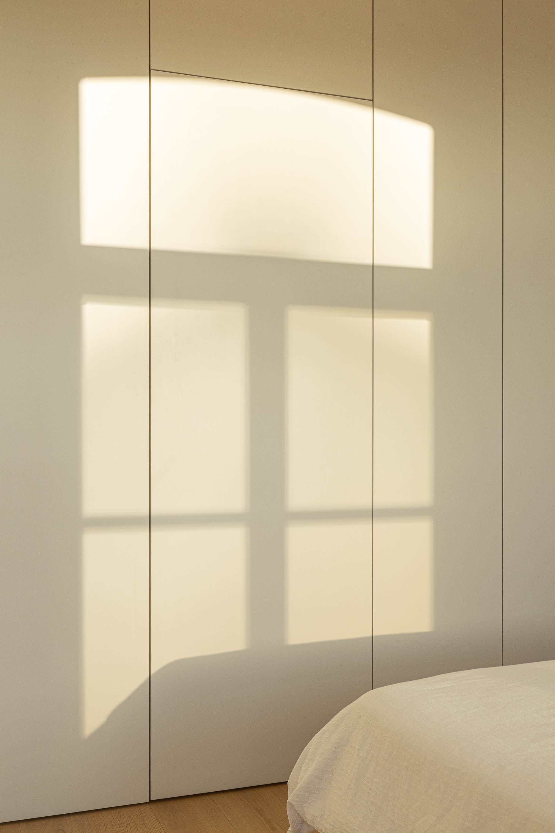 Quarto: Detalhe da parede com roupeiros embutidos brancos e sombra da janela. — Edifício de Mouzinho da Silveira arquitetura Diana Barros Arquitectura em Porto