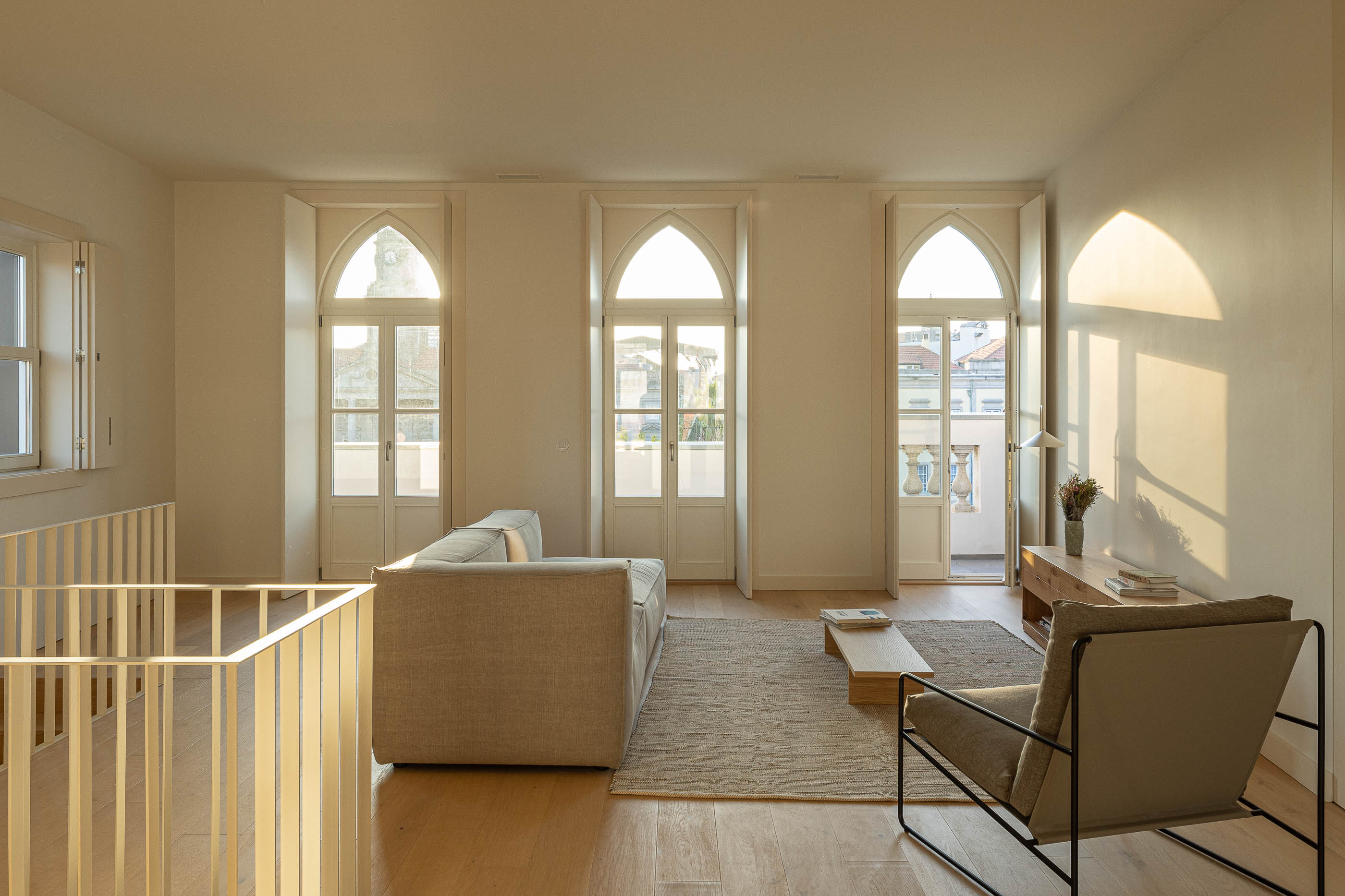 Sala de estar: Sala de estar com sofá cinzento, cadeiras e janelas em arco com acesso à varanda. — Edifício de Mouzinho da Silveira arquitetura Diana Barros Arquitectura em Porto