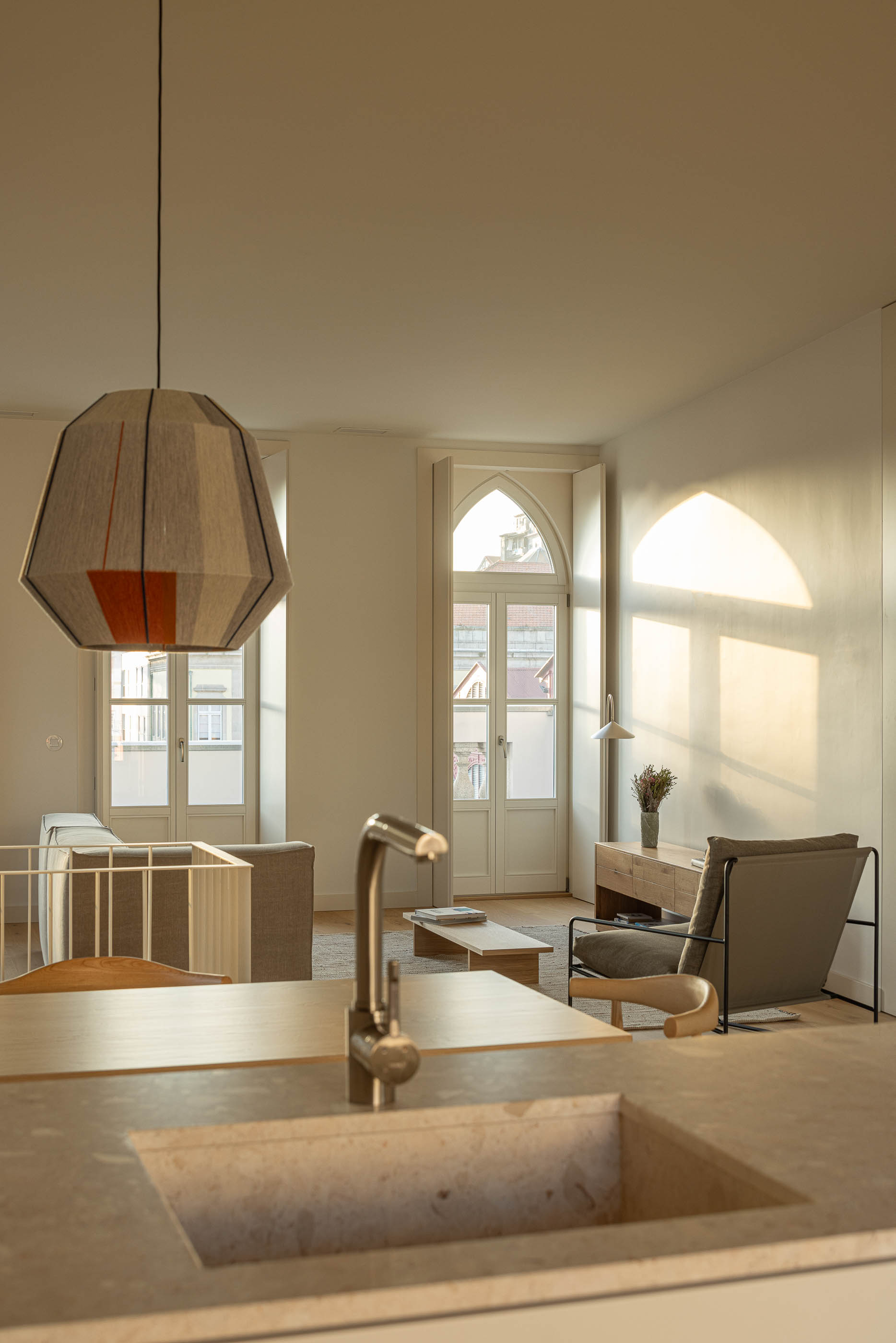 Sala de estar: Vista da sala de estar com candeeiro suspenso, sofá cinzento e lavatório em pedra. — Edifício de Mouzinho da Silveira arquitetura Diana Barros Arquitectura em Porto