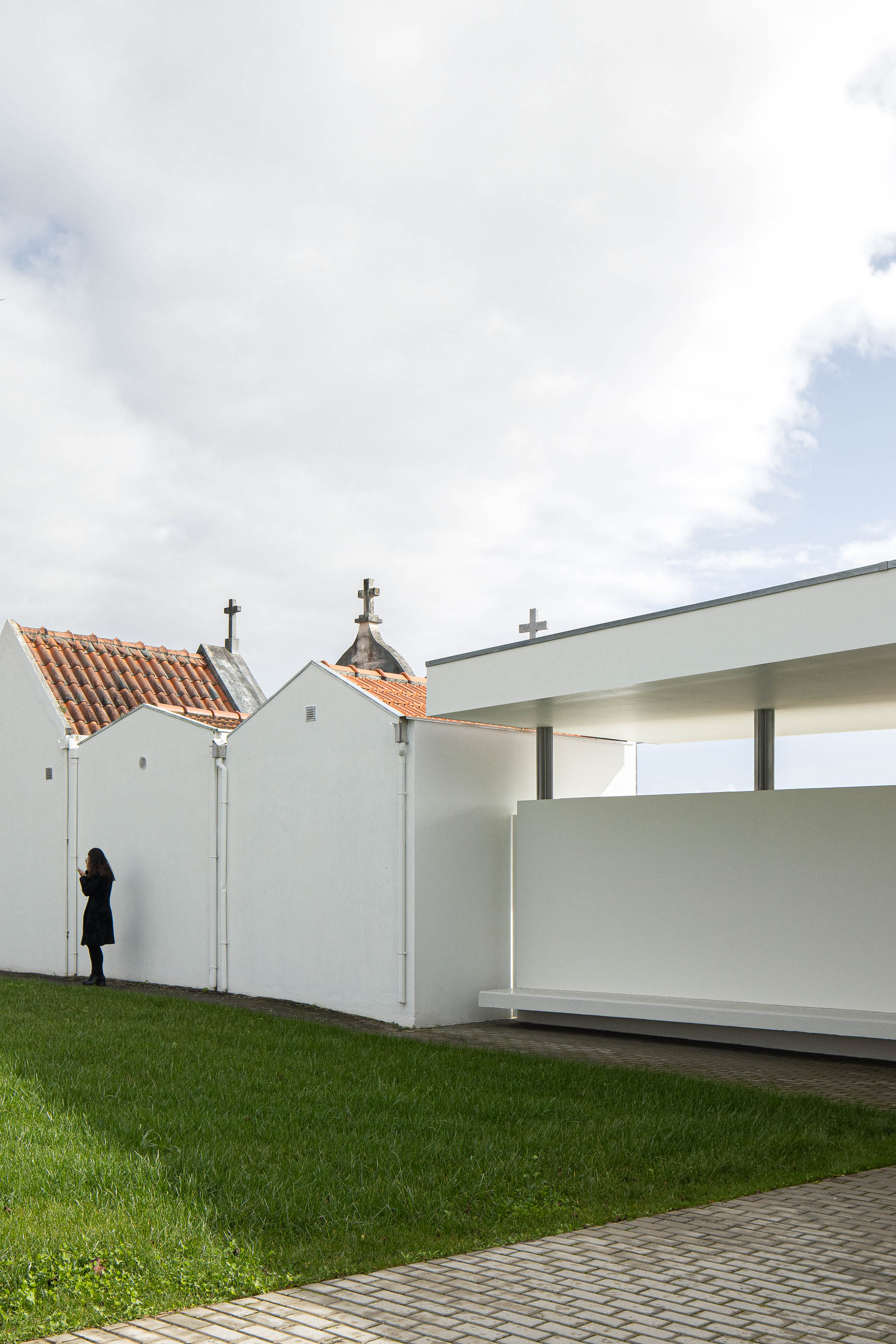 Exterior: Casa mortuária branca com alpendre, junto a capelas tradicionais e relvado. — Casa Mortuária de Oliveirinha arquitetura Sónia Cruz Arquitectura em Aveiro