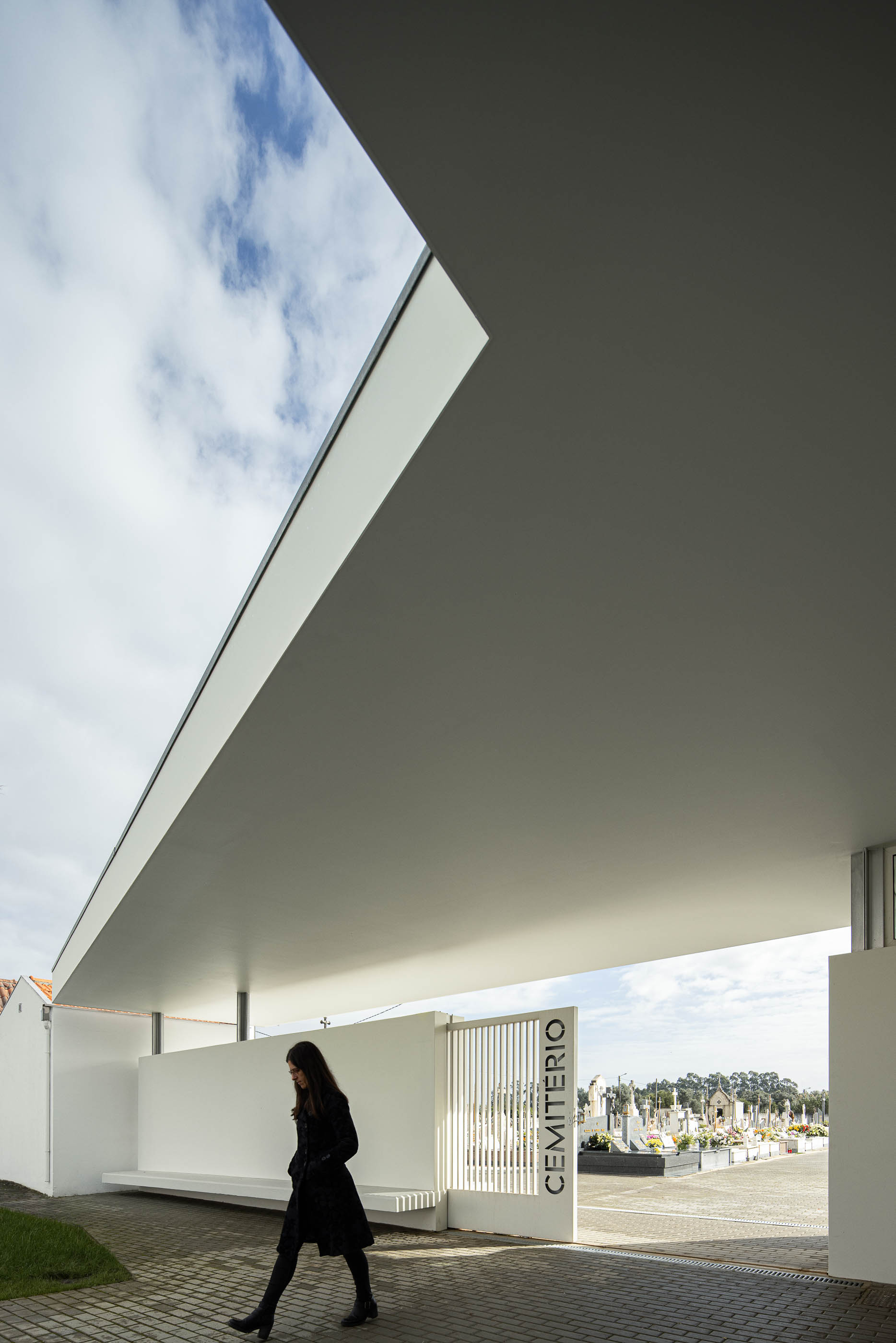 Exterior: Alpendre da casa mortuária com porta gradeada para o cemitério e teto inclinado. — Casa Mortuária de Oliveirinha arquitetura Sónia Cruz Arquitectura em Aveiro
