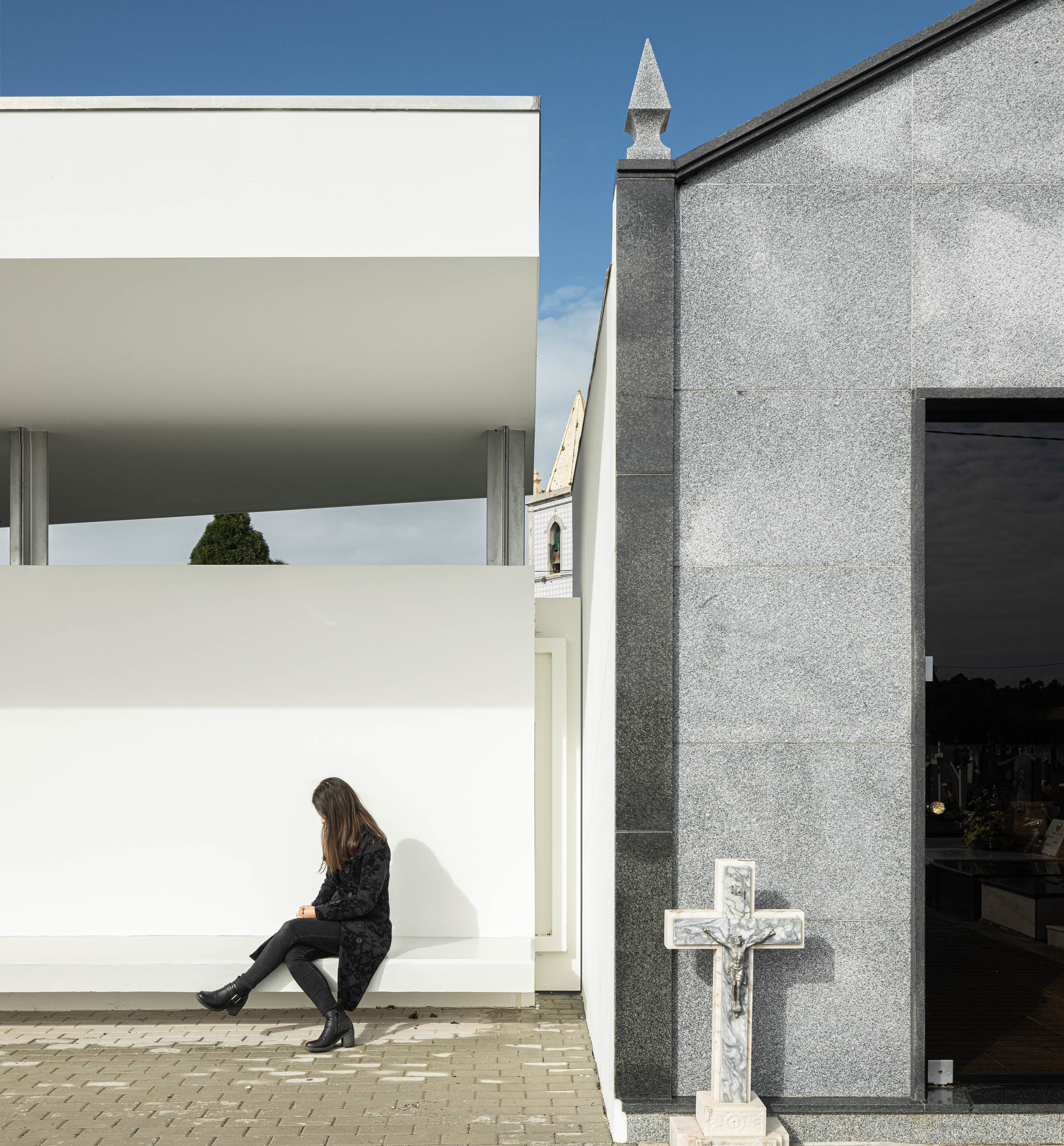 Exterior: Banco no alpendre da casa mortuária, com vista para o cemitério e capela em granito. — Casa Mortuária de Oliveirinha arquitetura Sónia Cruz Arquitectura em Aveiro