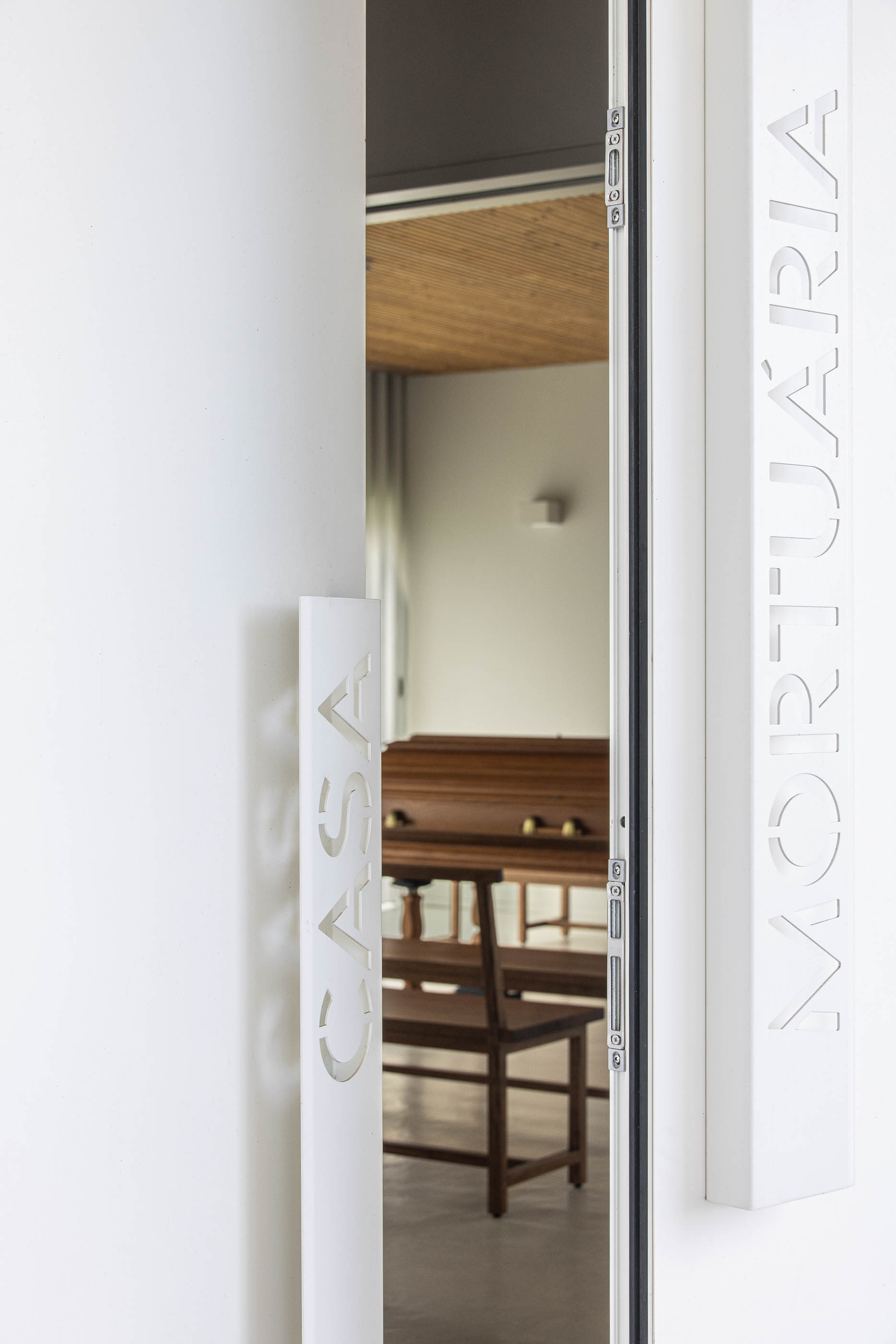 Entrada: Porta da casa mortuária com detalhe do puxador e vista para o interior com caixão. — Casa Mortuária de Oliveirinha arquitetura Sónia Cruz Arquitectura em Aveiro