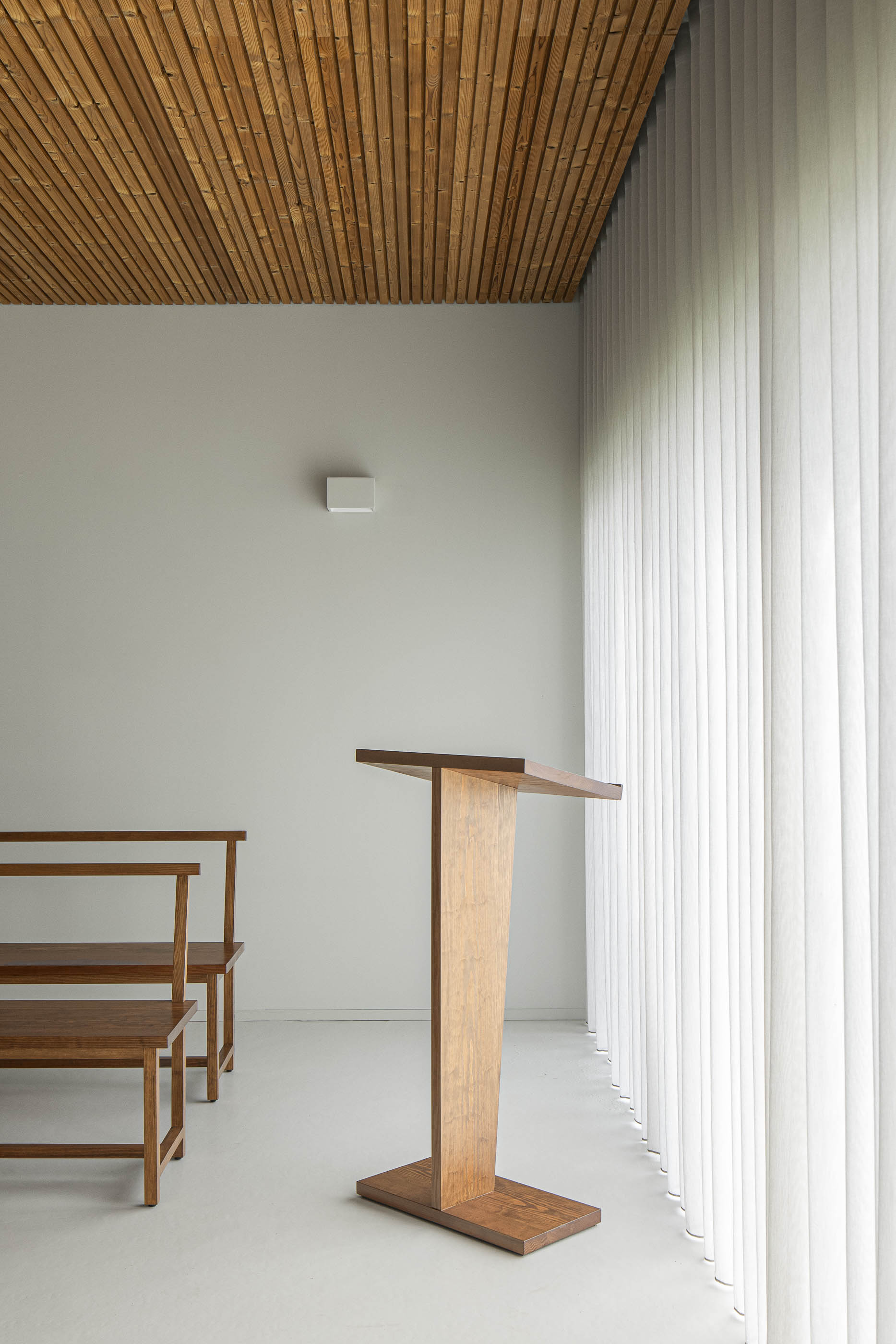 Interior: Púlpito de madeira na sala de cerimónias, com teto em madeira e cortinas verticais. — Casa Mortuária de Oliveirinha arquitetura Sónia Cruz Arquitectura em Aveiro