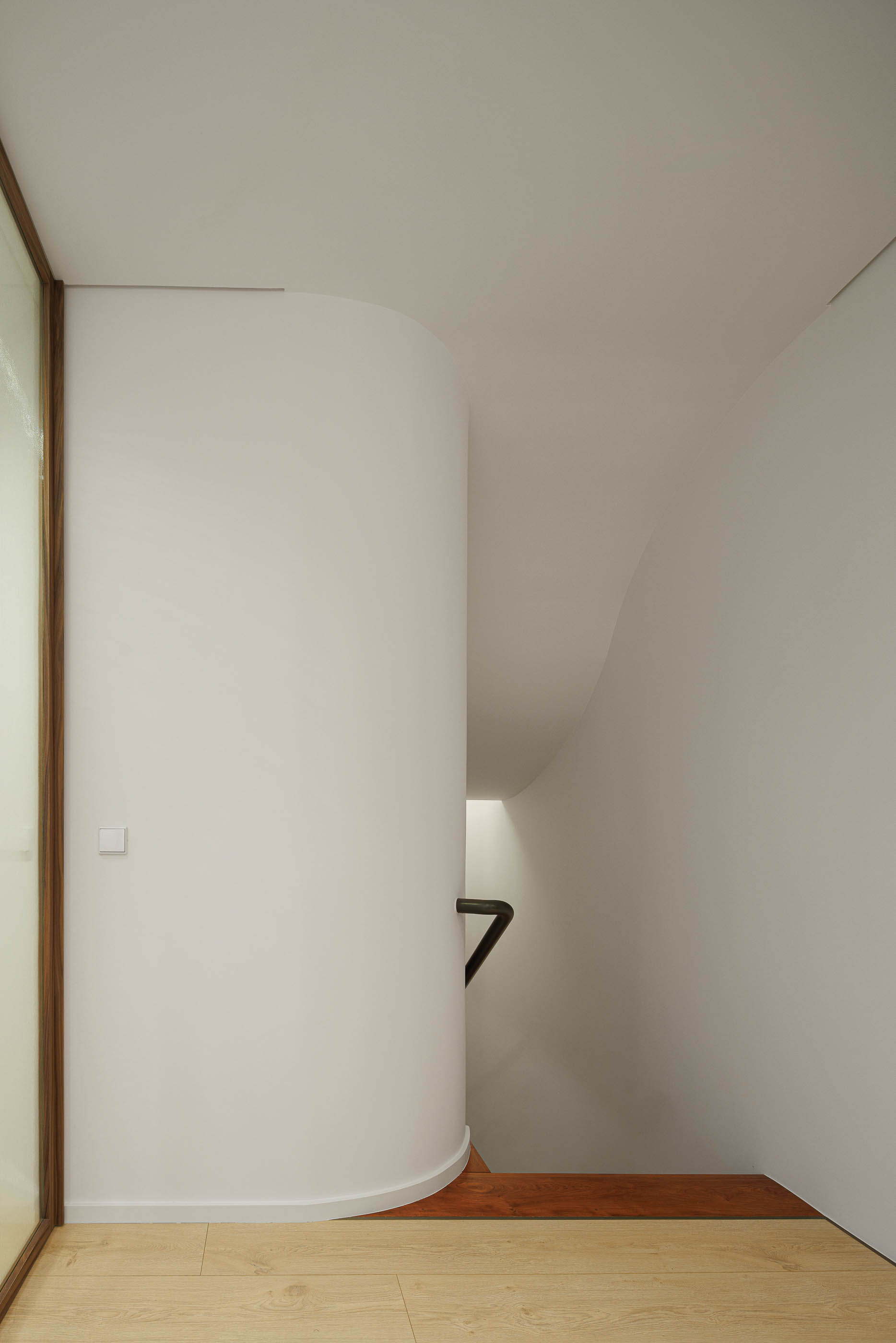 Escada: Detalhe da curva da escada com paredes brancas e pavimento em madeira clara e escura. — Corujeira 113 arquitetura Impare Arquitectura em Porto