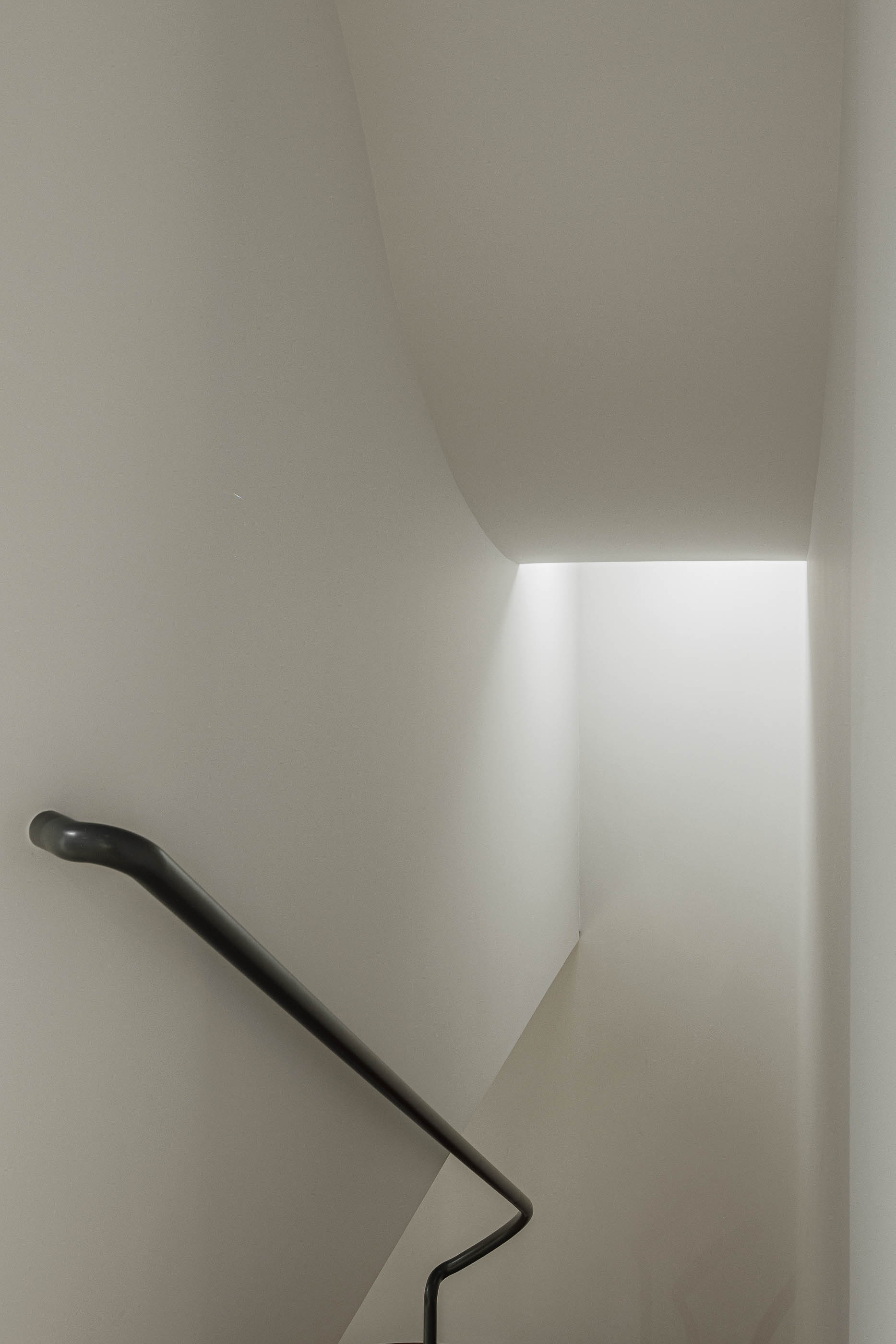 Escada: Vista ascendente da escada com corrimão preto e paredes brancas, iluminação zenital. — Corujeira 113 arquitetura Impare Arquitectura em Porto
