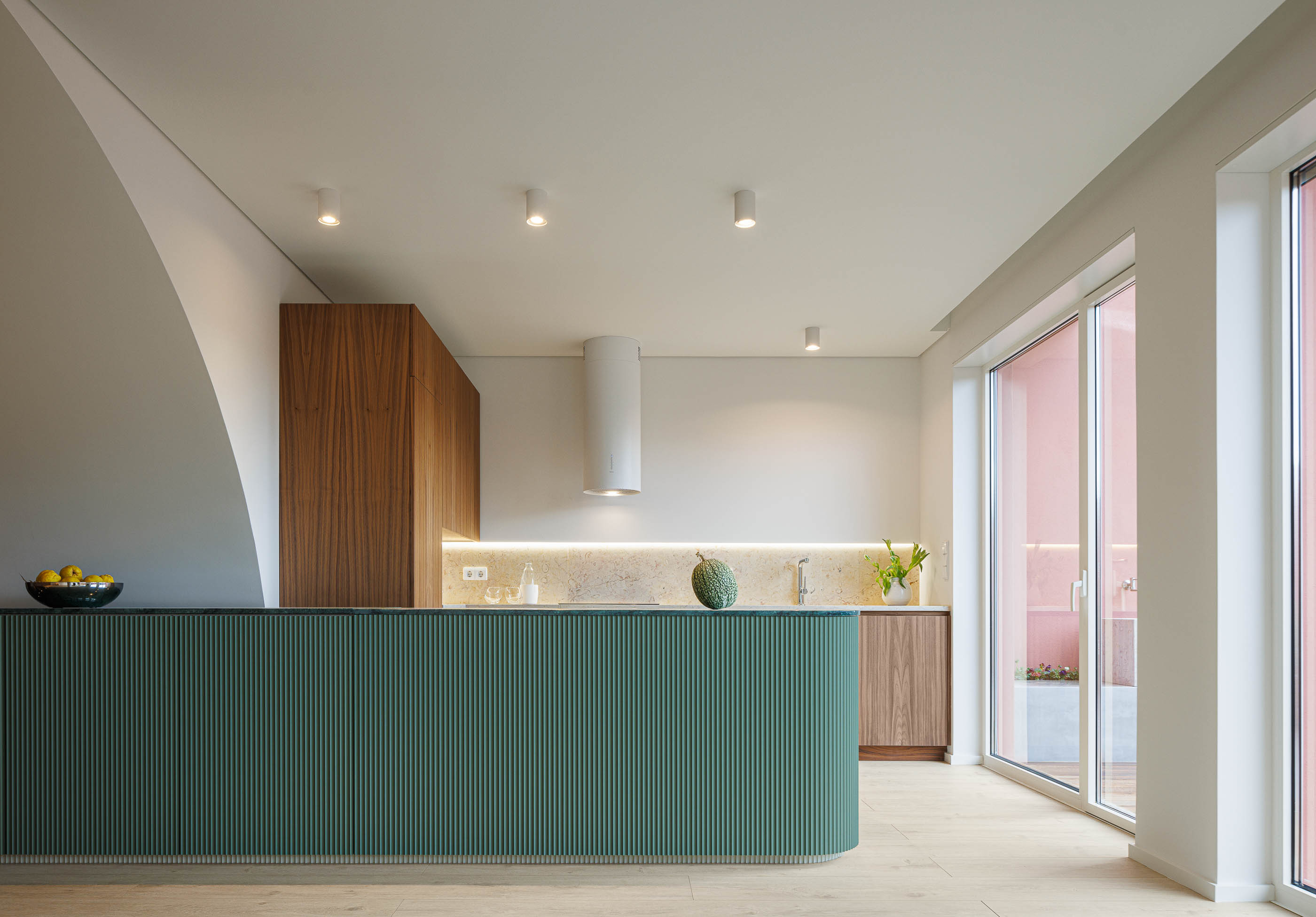 Cozinha: Vista geral da cozinha com ilha verde canelada, armários em madeira, pavimento em madeira clara e acesso ao terraço. — Corujeira 113 arquitetura Impare Arquitectura em Porto