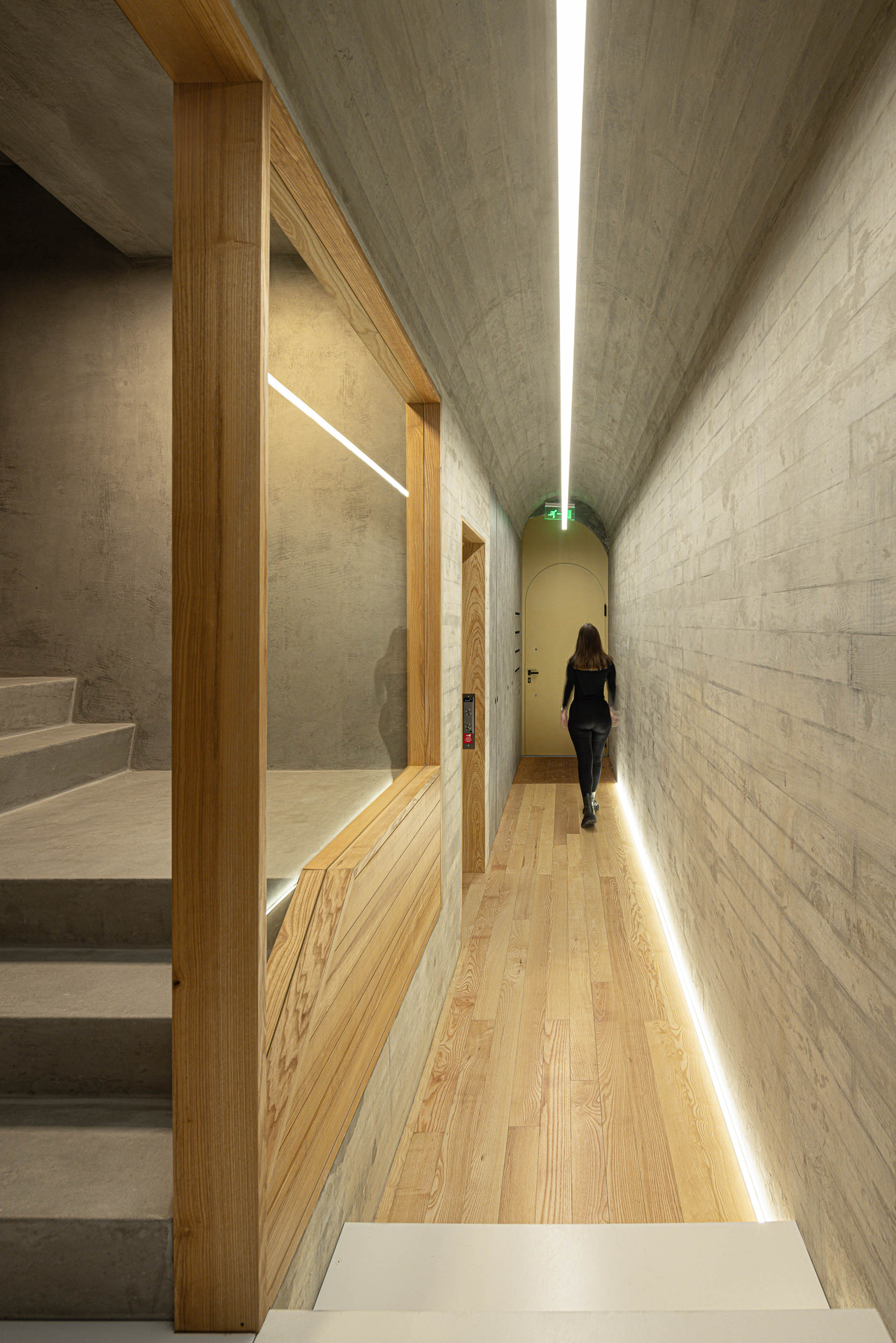 Corredor com pavimento em madeira, iluminação linear e escadas em betão à esquerda. — Boavista 339 arquitetura Paulo Merlini Architects em Porto