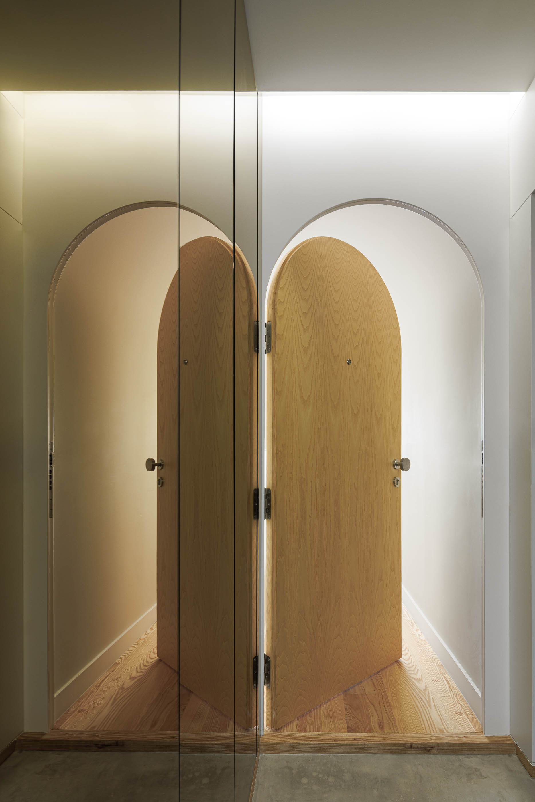 Portas em arco de madeira clara, refletidas num espelho, com iluminação superior suave. — Boavista 339 arquitetura Paulo Merlini Architects em Porto
