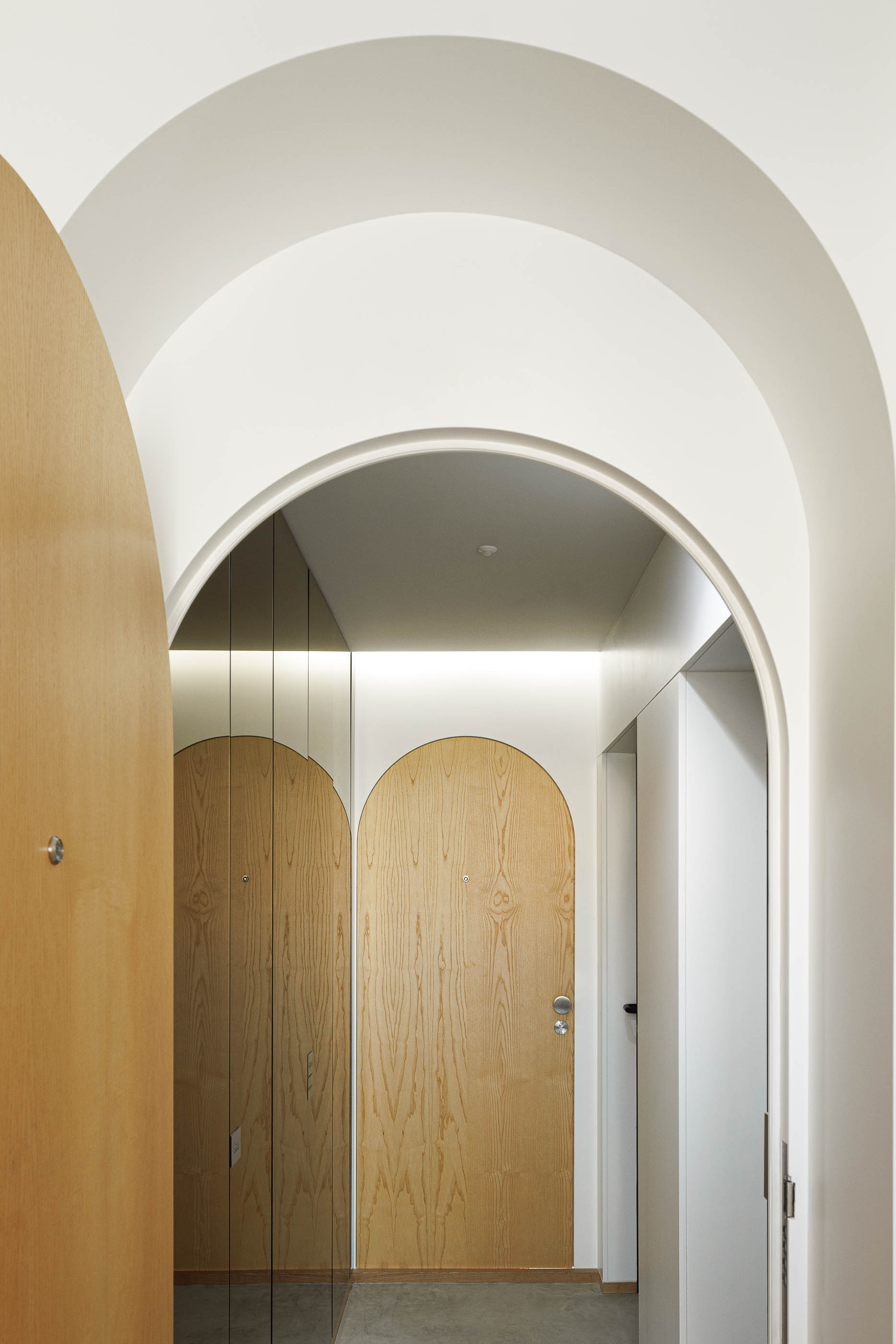 Vista interior de portas em arco, com espelho e iluminação, criando uma perspetiva alongada. — Boavista 339 arquitetura Paulo Merlini Architects em Porto