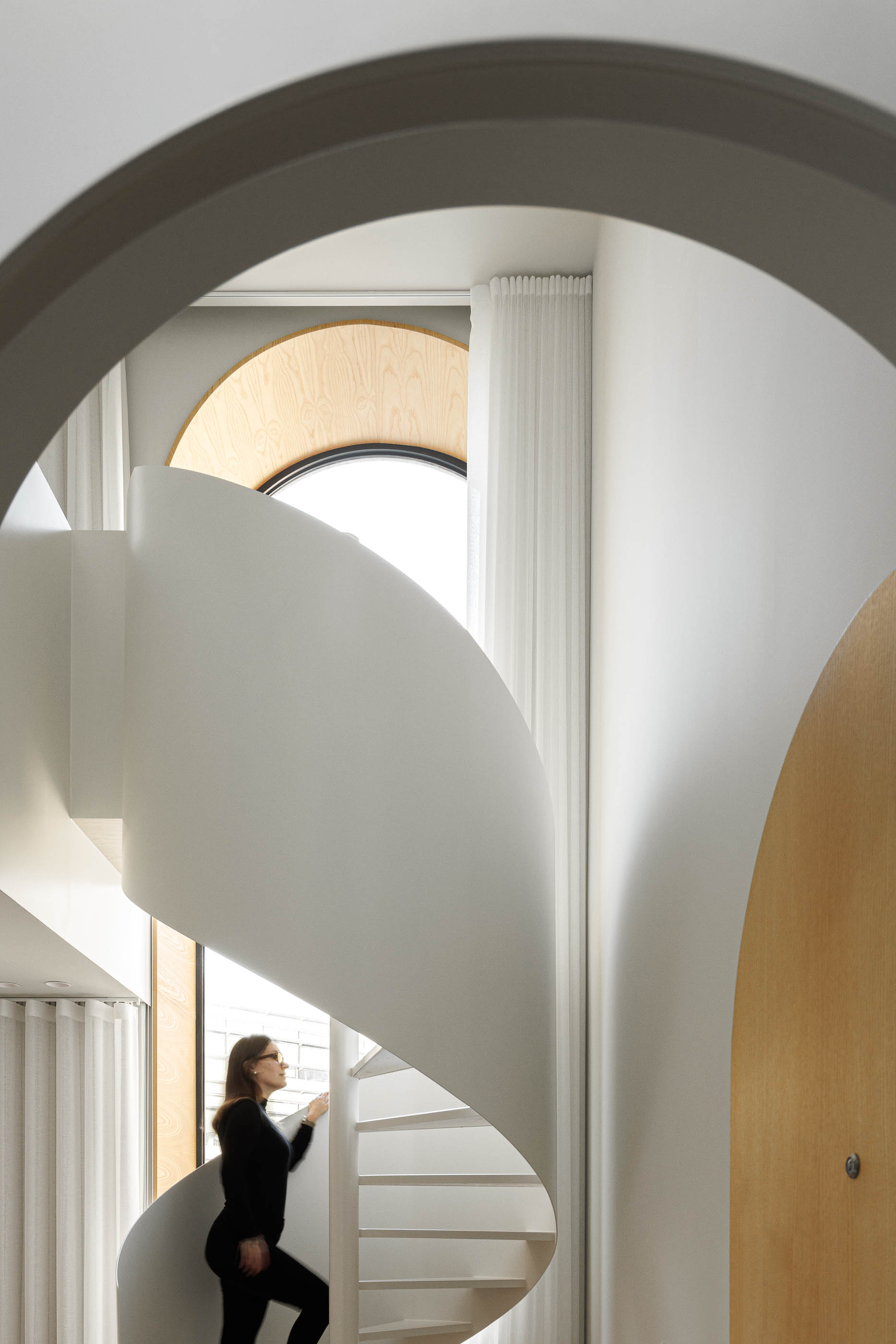 Mulher a subir a escada em caracol branca, vista através de uma porta em arco. — Boavista 339 arquitetura Paulo Merlini Architects em Porto