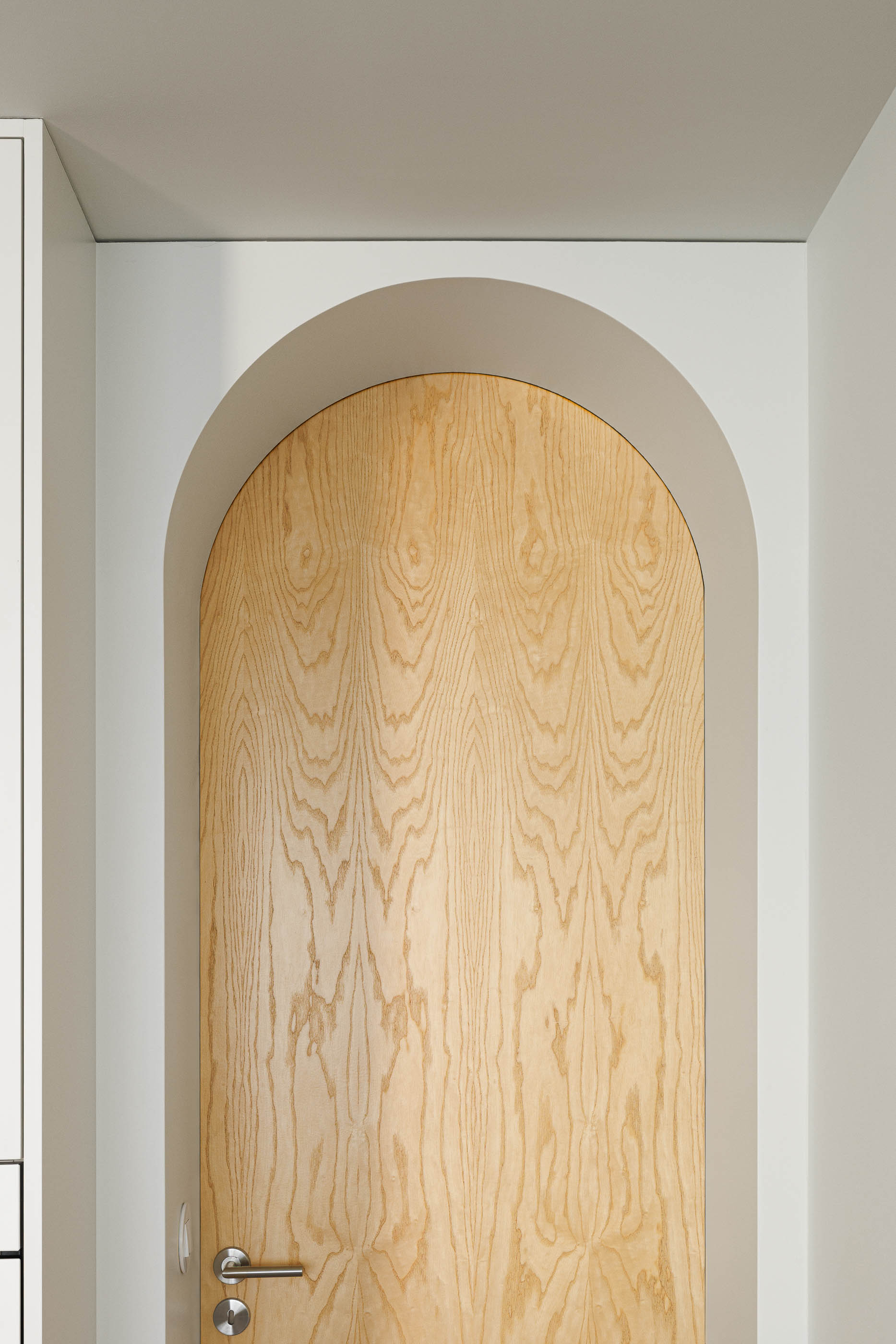 Detalhe de uma porta em arco em madeira clara, com puxador metálico e parede branca. — Boavista 339 arquitetura Paulo Merlini Architects em Porto